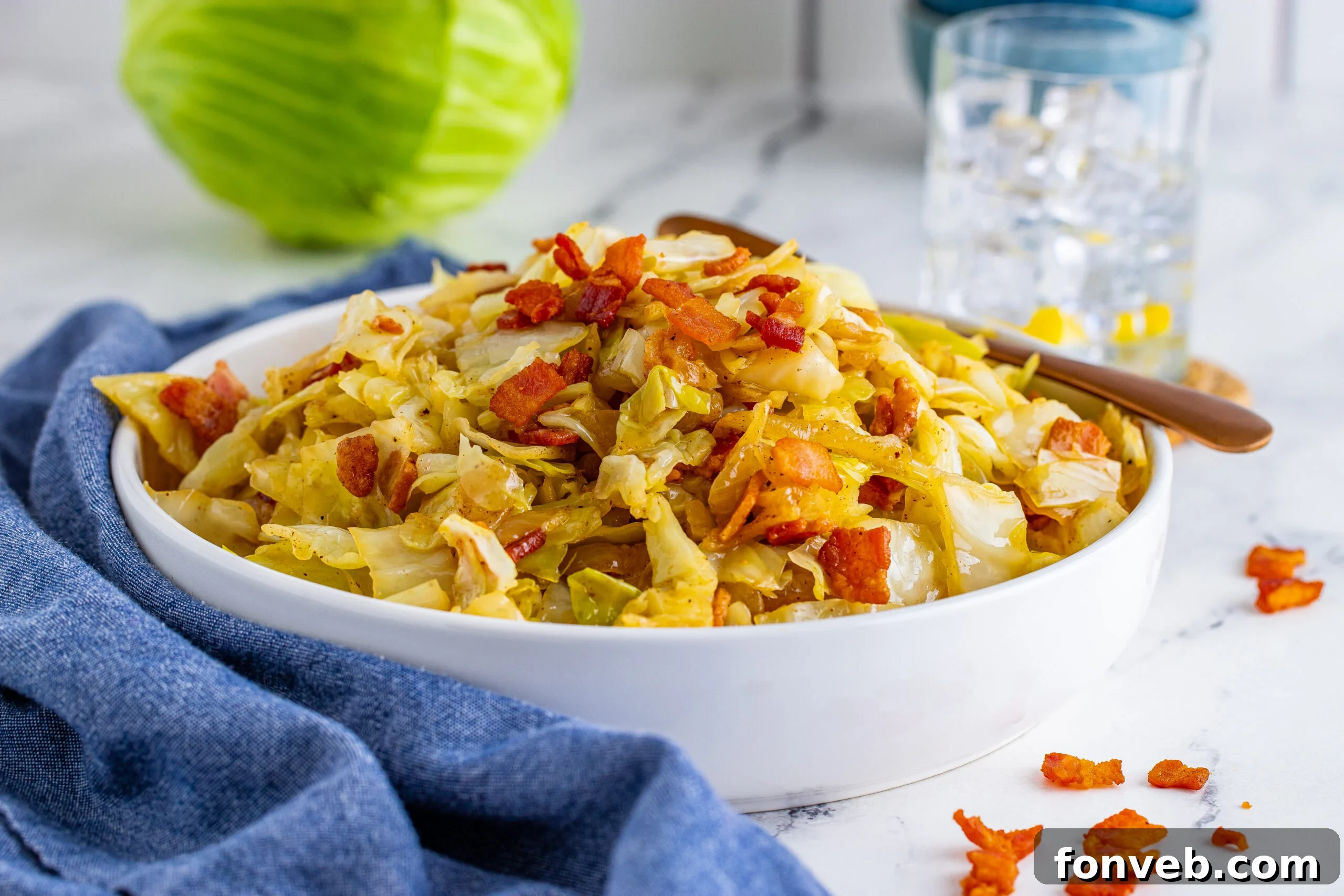Horizontal image of bacon fried cabbage in a white bowl with a navy linen. 