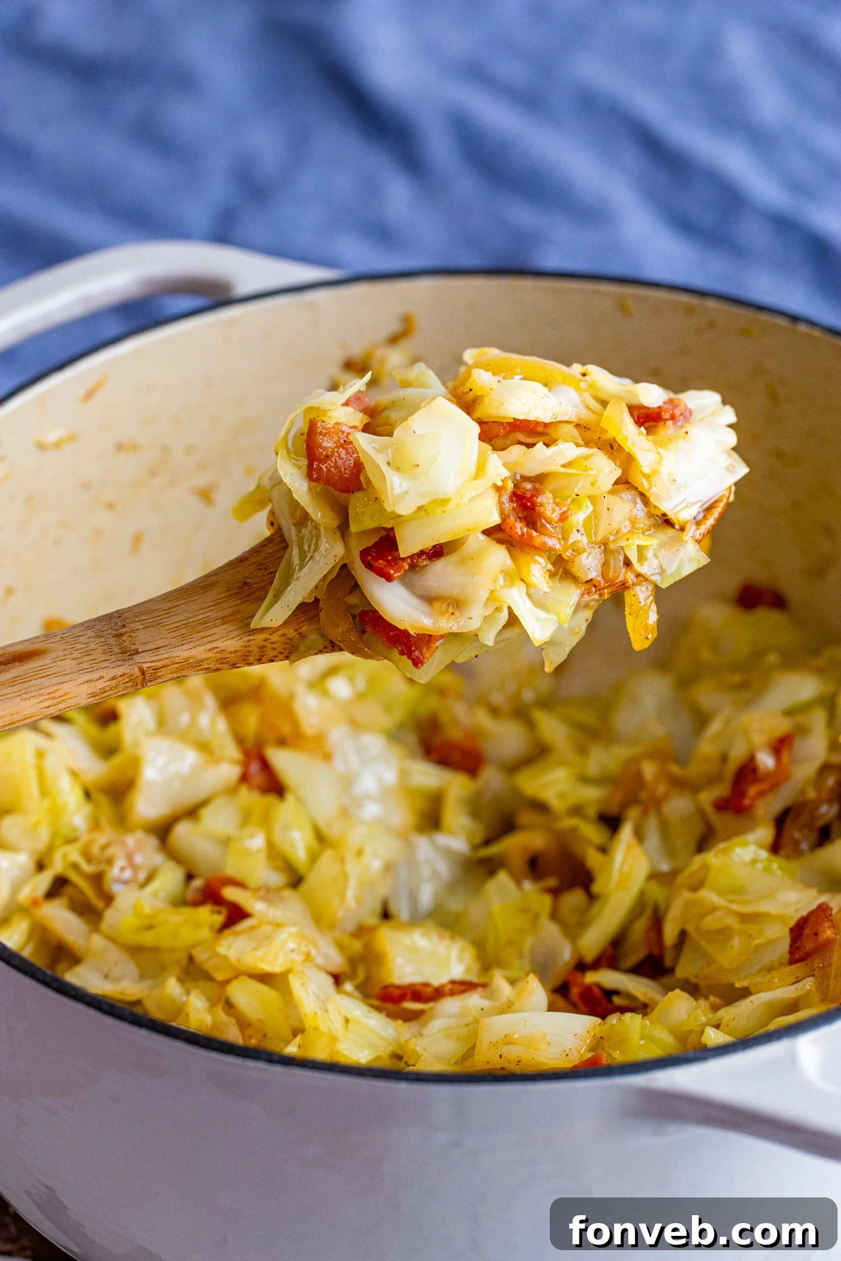 Fried cabbage being removed with a wooden spoon from a large Dutch oven. 