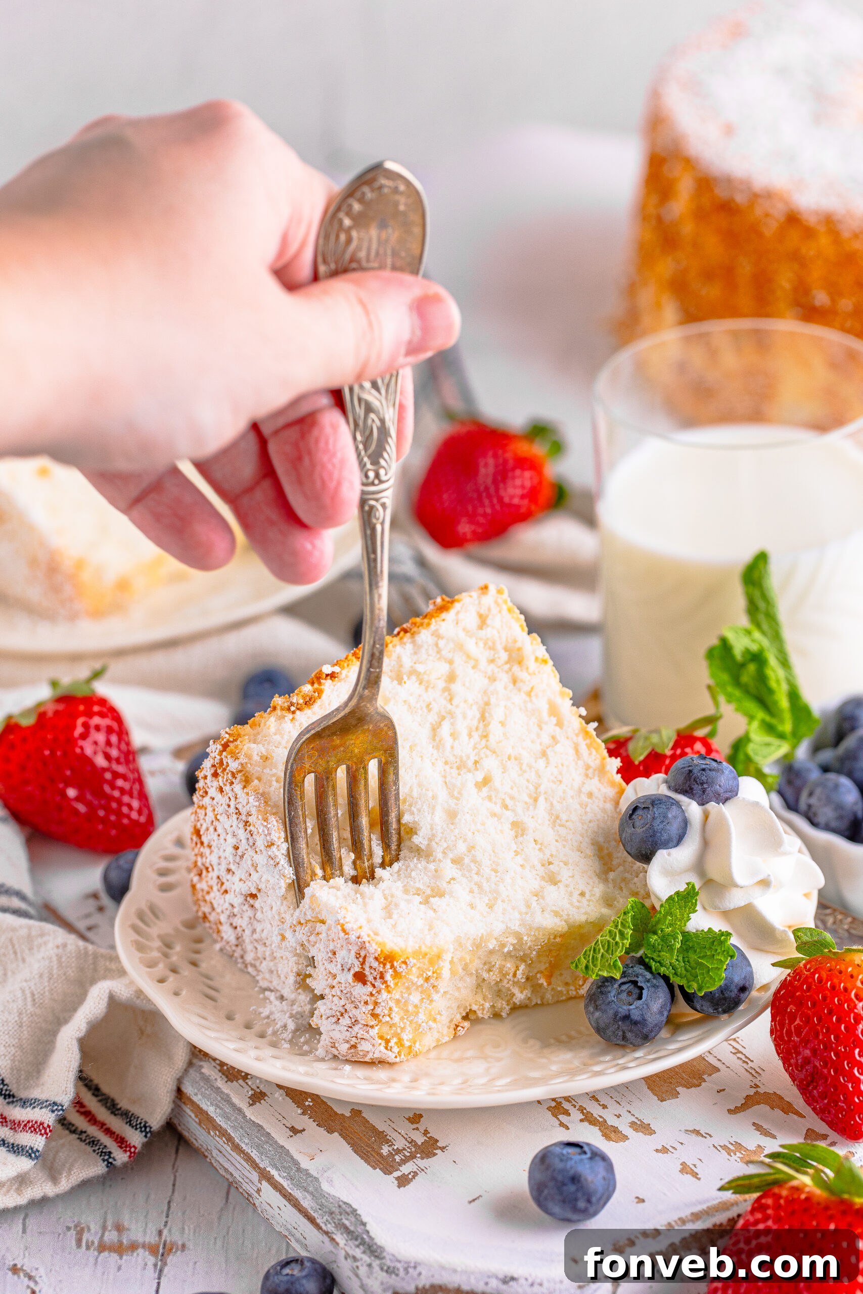 A fork taking a delicate bite from a slice of Angel Food Cake, highlighting its soft, inviting texture.