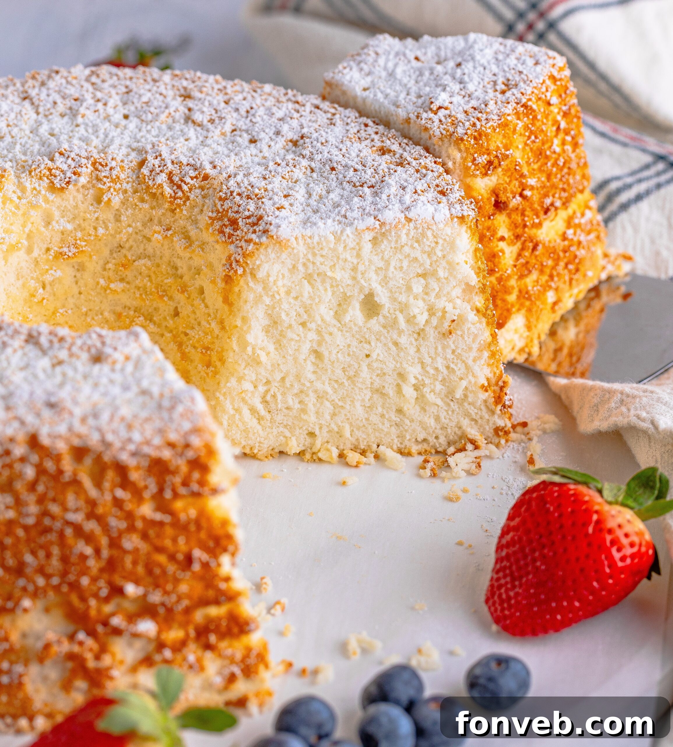 A beautifully presented Angel Food Cake on a white serving platter with one slice already removed, ready to be enjoyed.