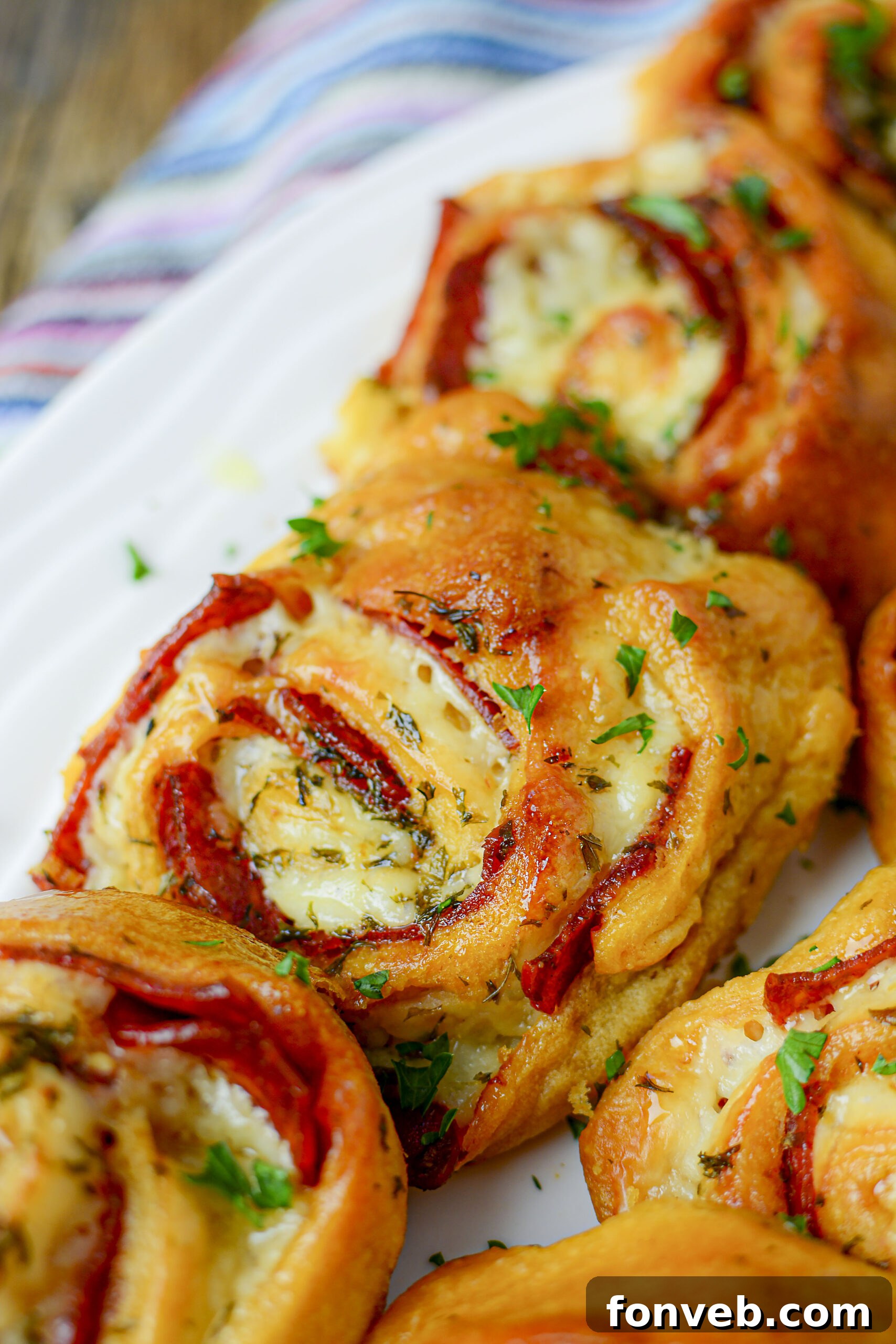 Swirled Pizza Bites 14 A row of baked pizza pinwheels on a white plate, showcasing their golden crust.