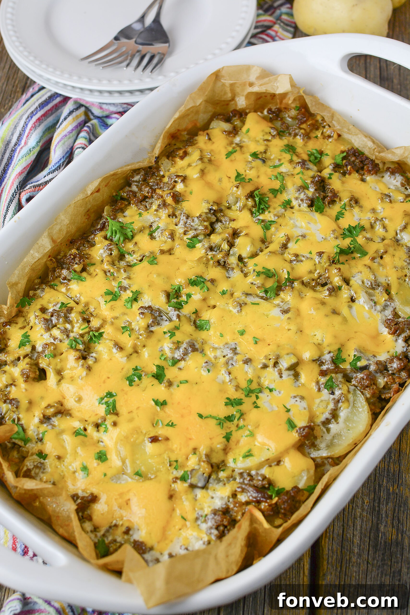 Golden Cheesy Beef and Potato Bake 2 Golden-brown Cheesy Ground Beef and Potato Casserole in a white baking dish, garnished with fresh parsley.