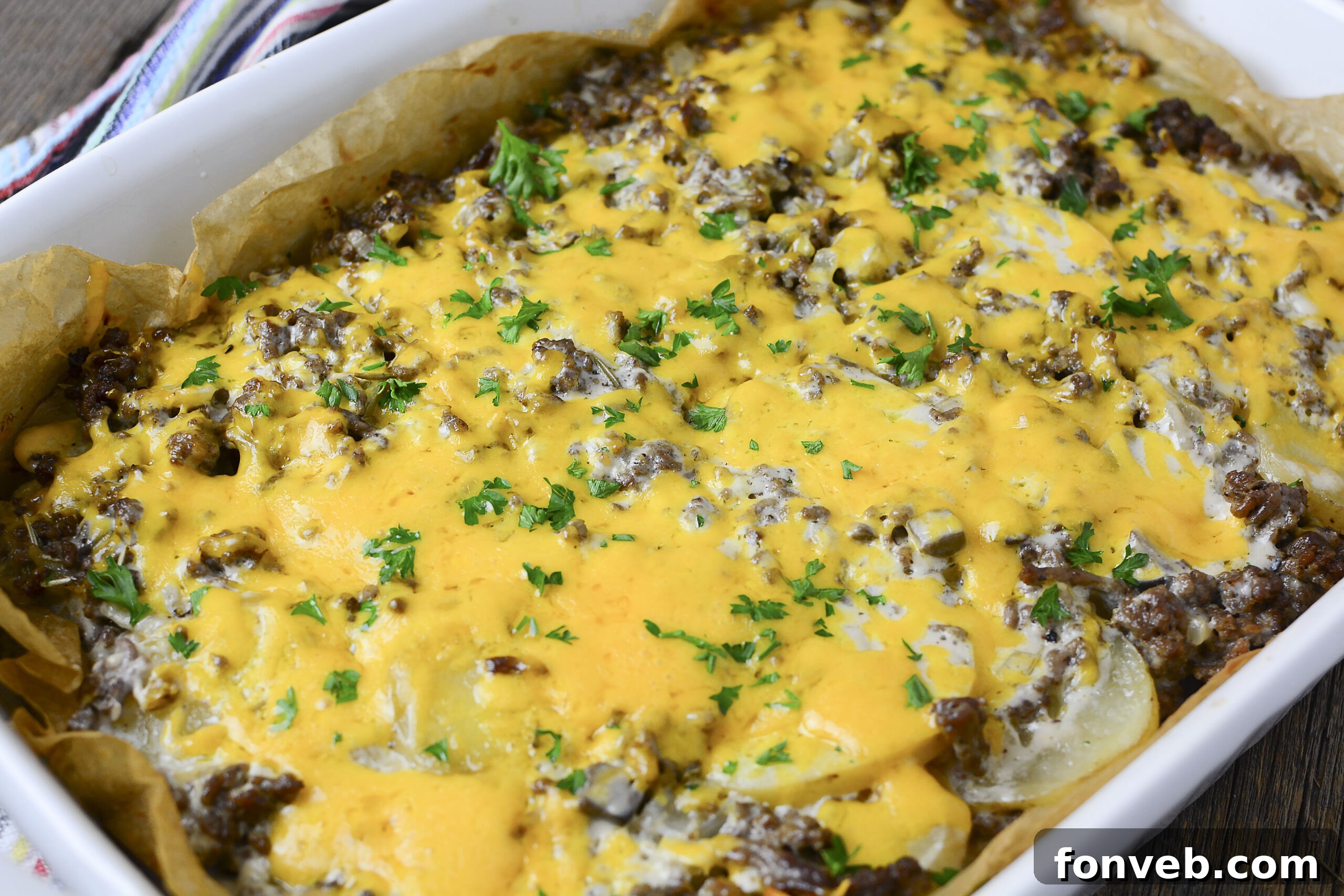 Golden Cheesy Beef and Potato Bake 13 Close-up of a richly cheesy Ground Beef and Potato Casserole in a white dish, garnished with parsley and bubbling with melted cheese.