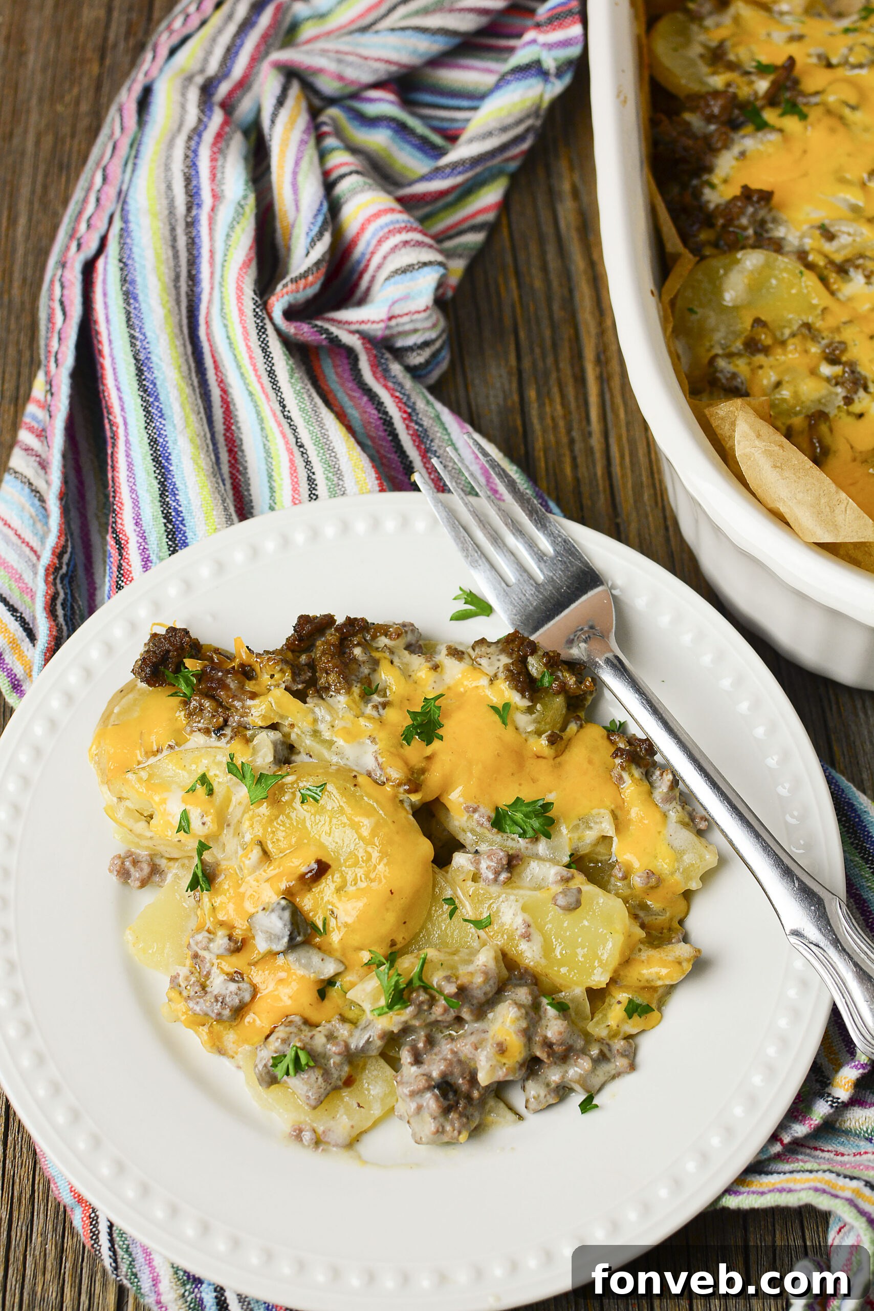 Golden Cheesy Beef and Potato Bake 3 A serving of Cheesy Ground Beef and Potato Casserole on a white plate, topped with fresh green parsley.