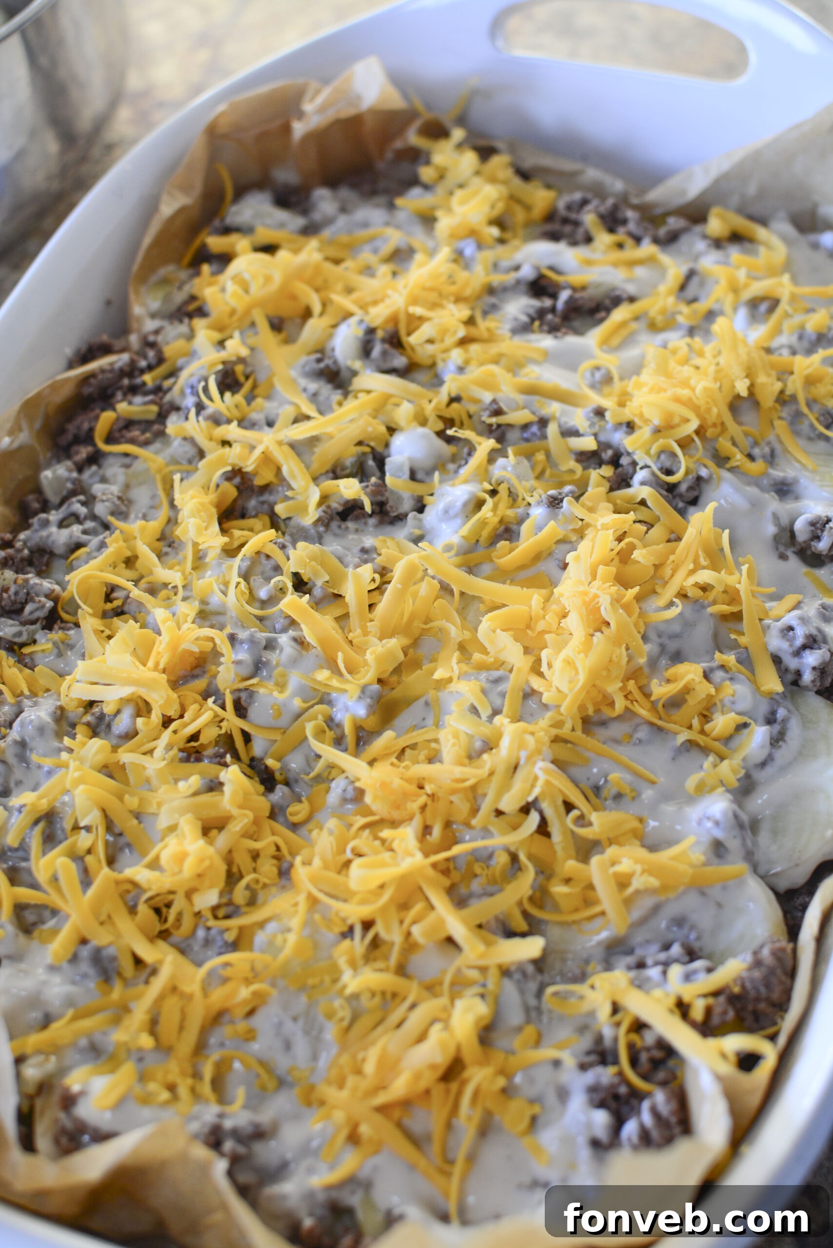 Golden Cheesy Beef and Potato Bake 10 Ground beef and onion mixture being spread over a layer of potatoes in a baking dish.