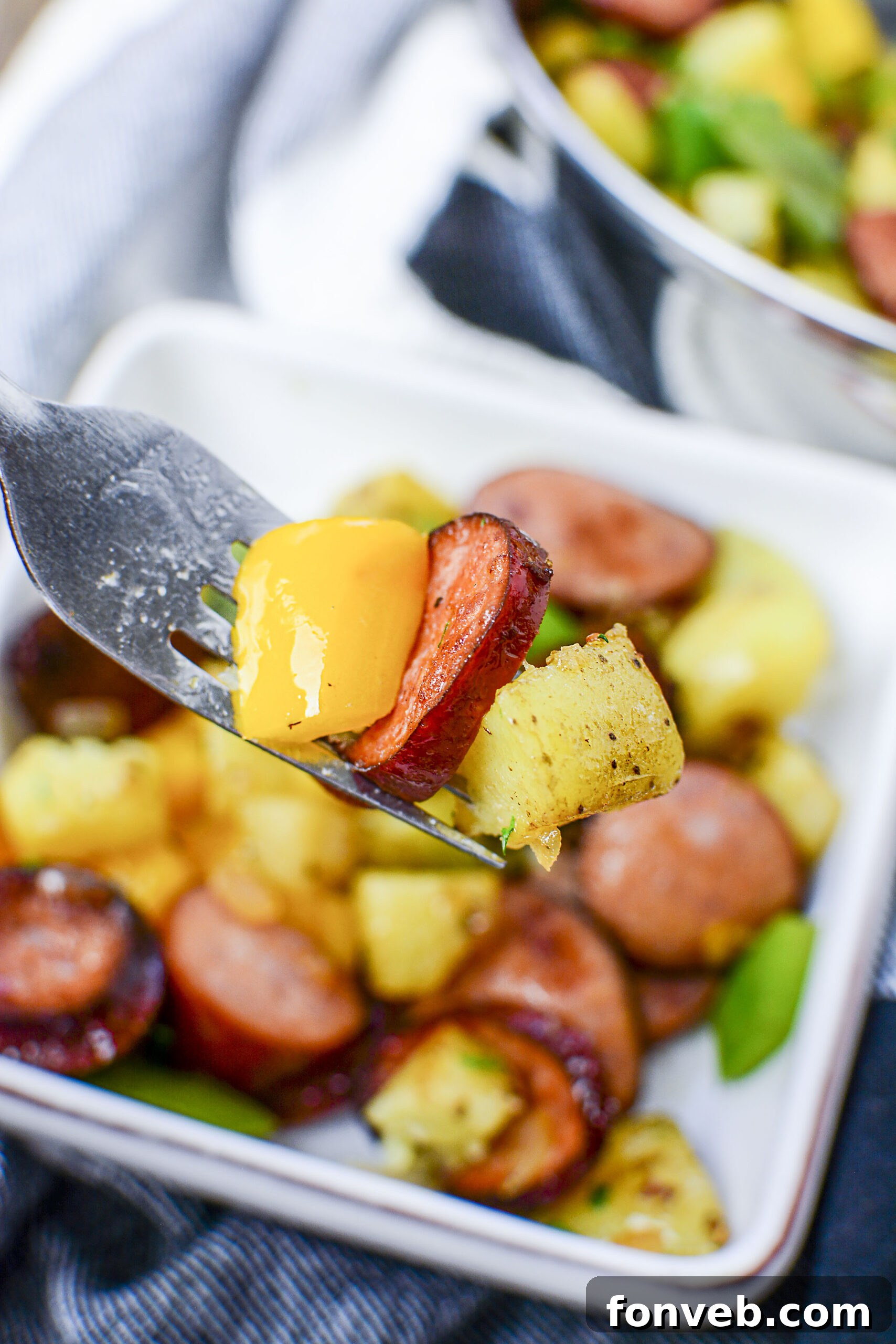 close up of sausage peppers and potatoes on a silver fork. 