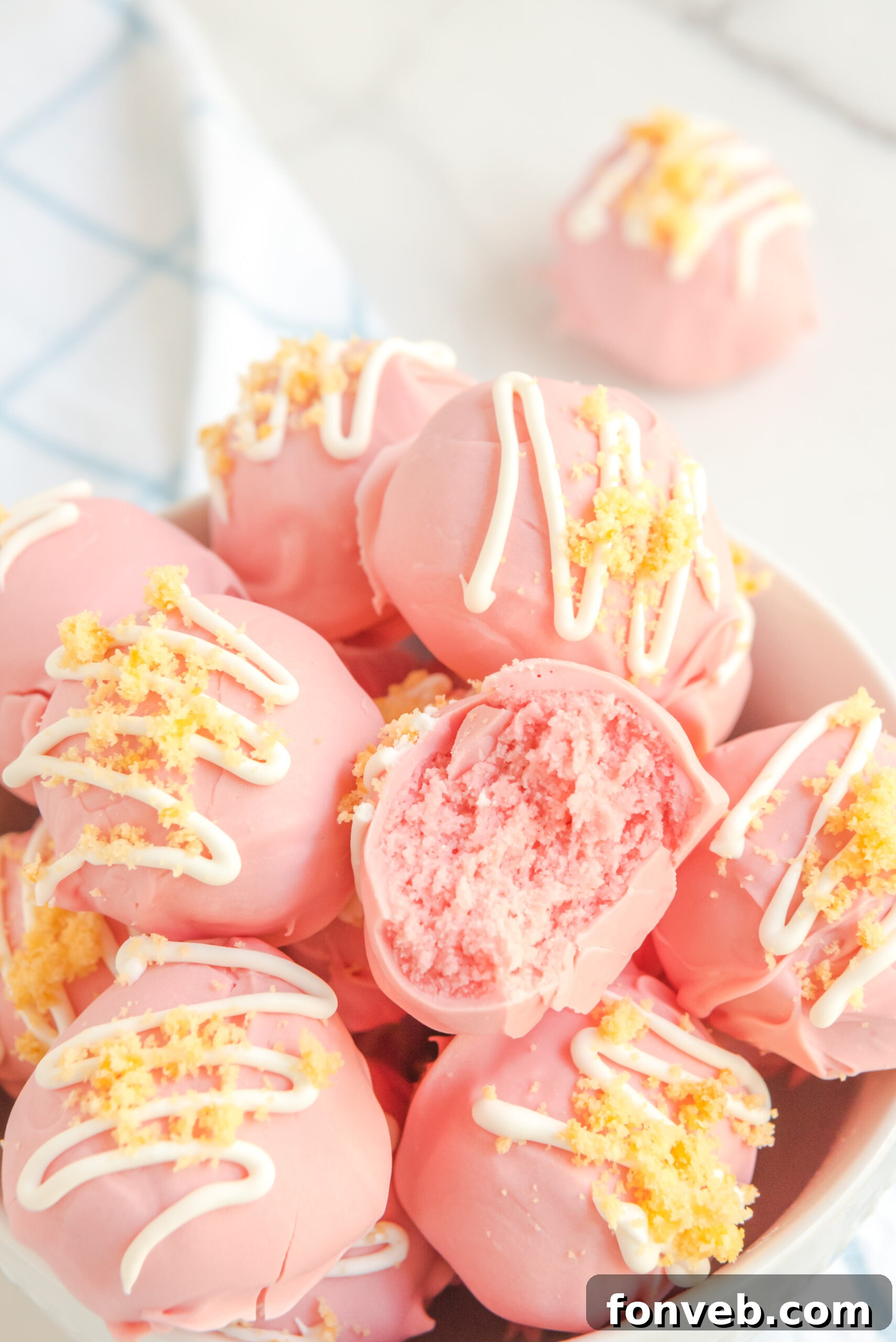 Strawberry truffles stacked on top of each other in a white bowl with a bite gone out of one