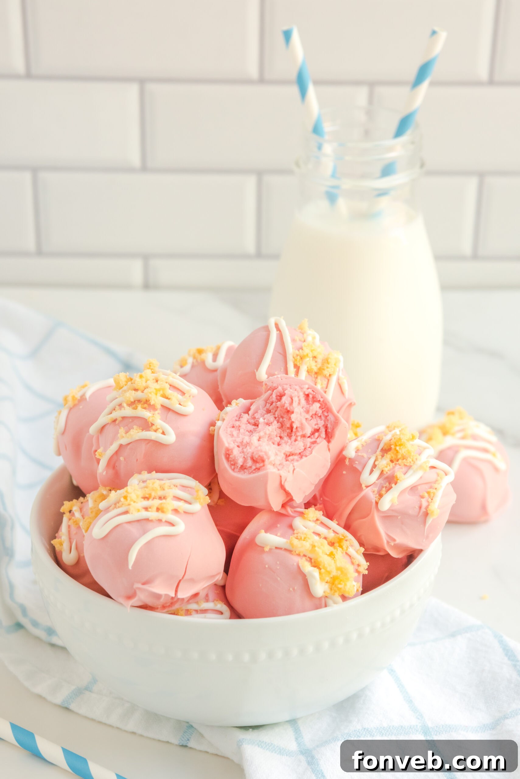 Strawberry truffles stacked on top of each other in a white bowl with milk and blue and white straws in the background.