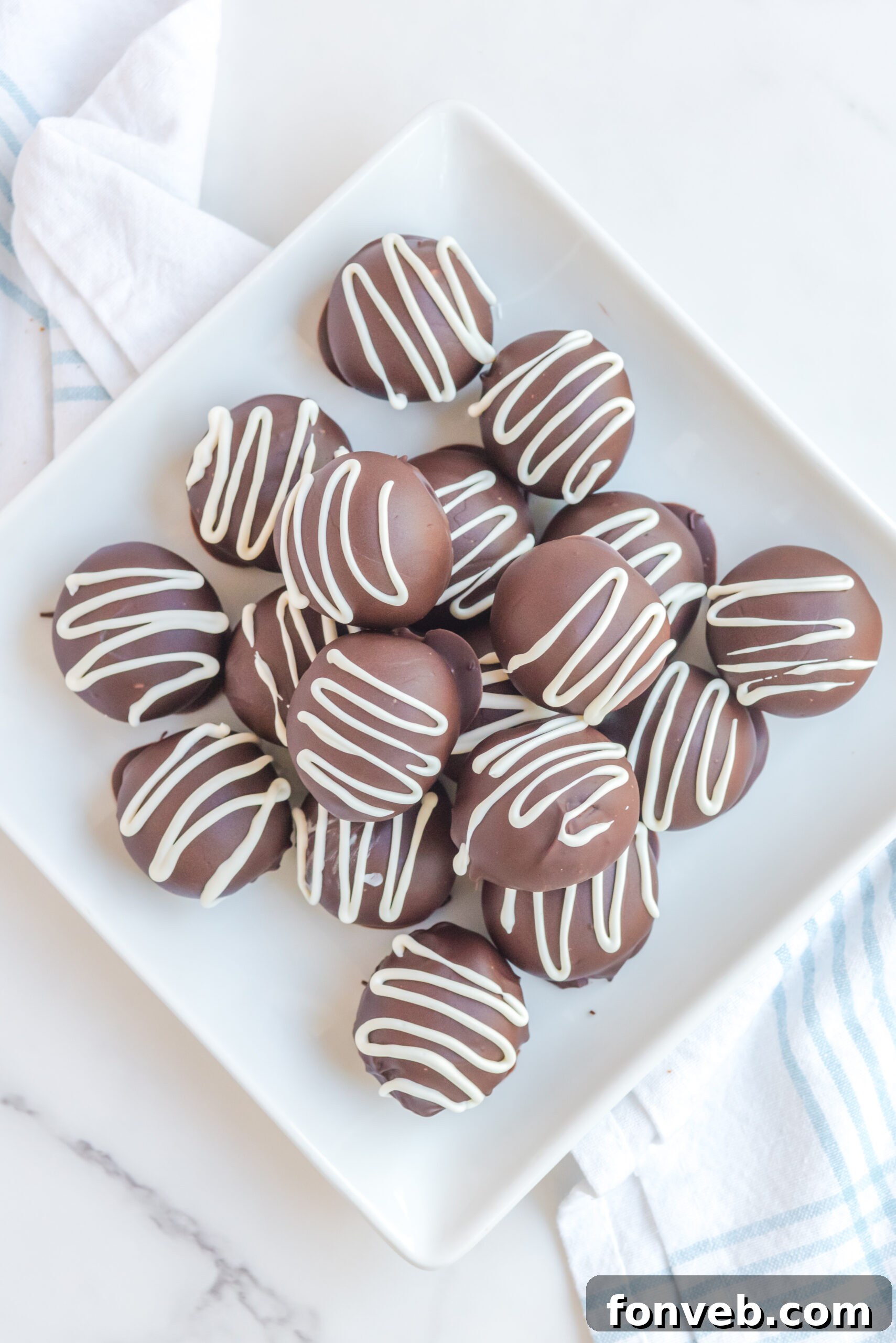 Decadent Brownie Bites 12 Brownie Truffles stacked on a white plate with brownies in the background.