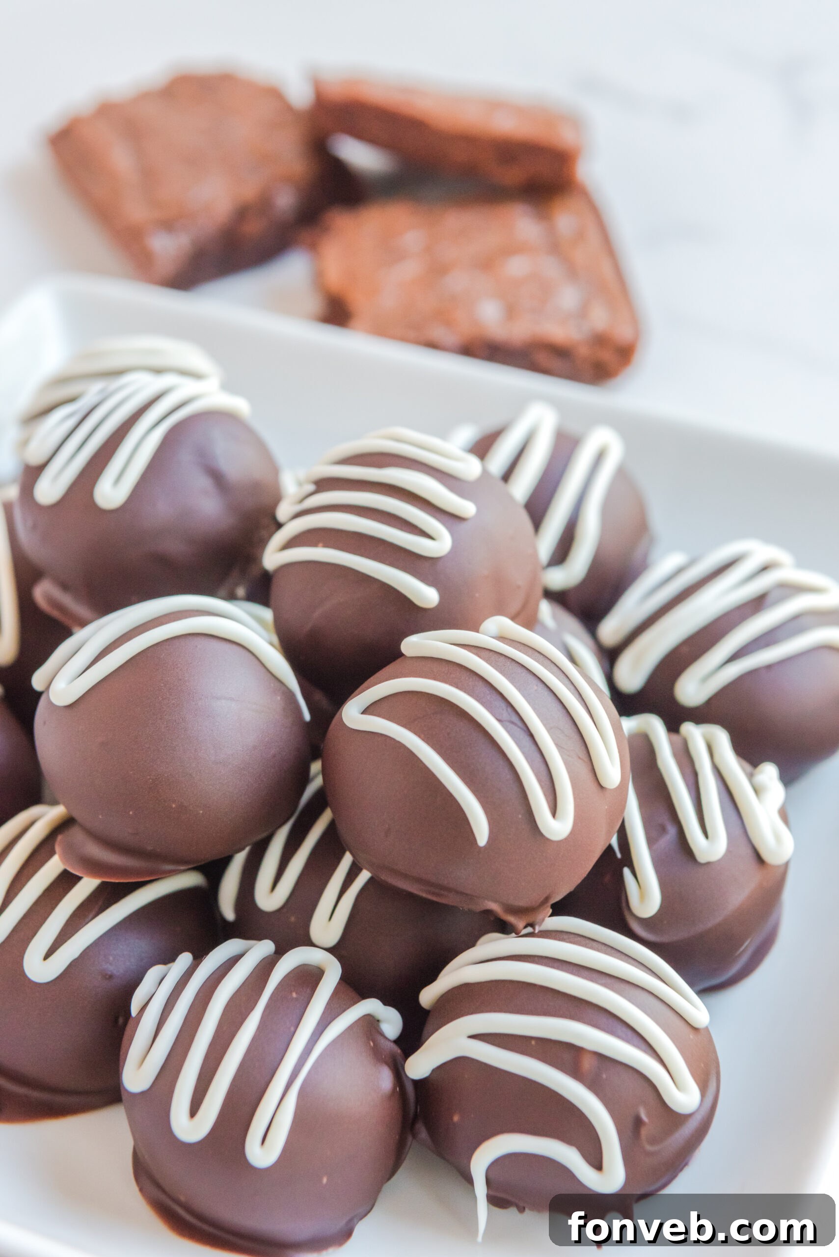 Decadent Brownie Bites 3 Brownie Bite Truffles on a white plate with brownies stacked behind them