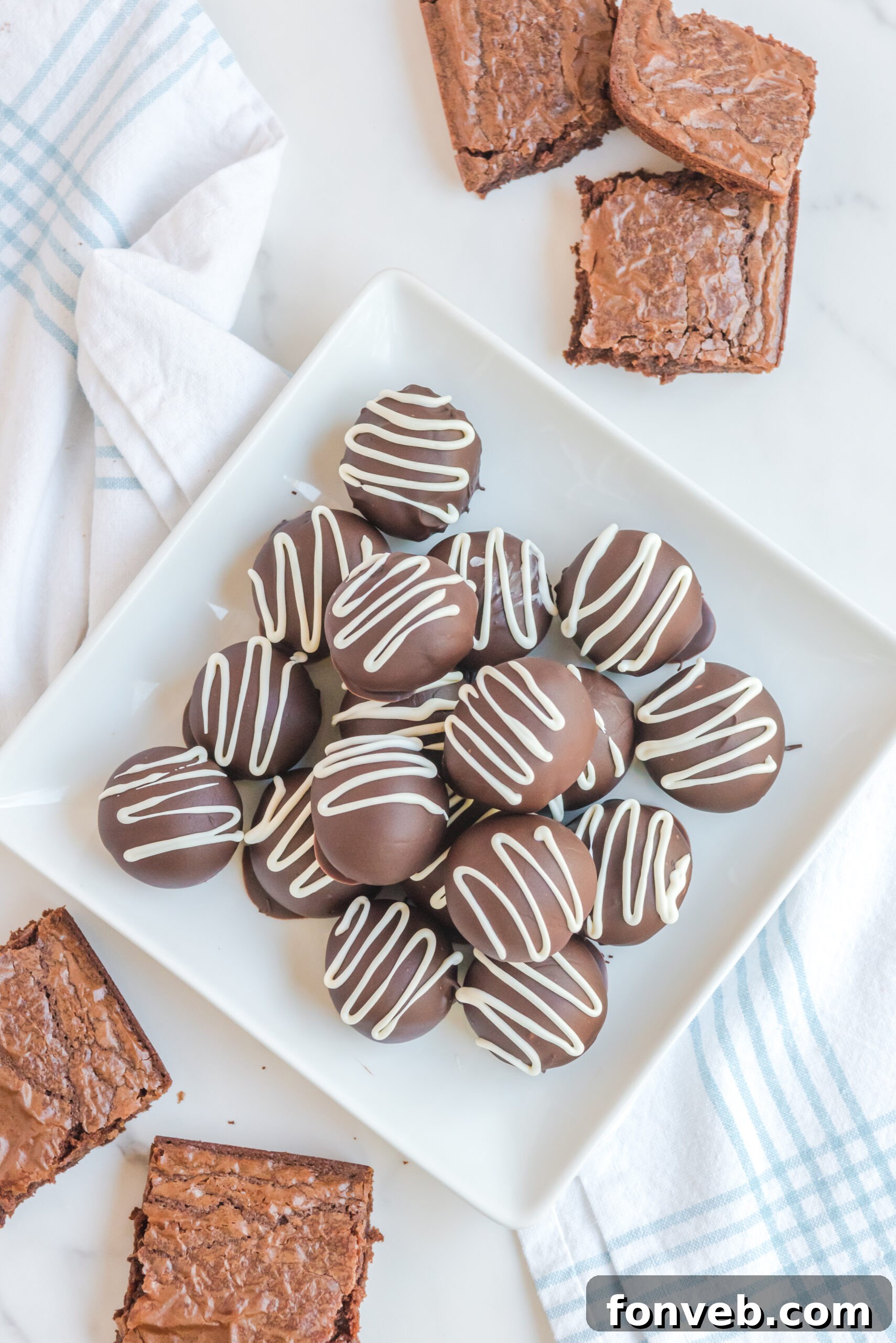 Decadent Brownie Bites 4 Brownie Truffles stacked on a white plate with brownies in the background.