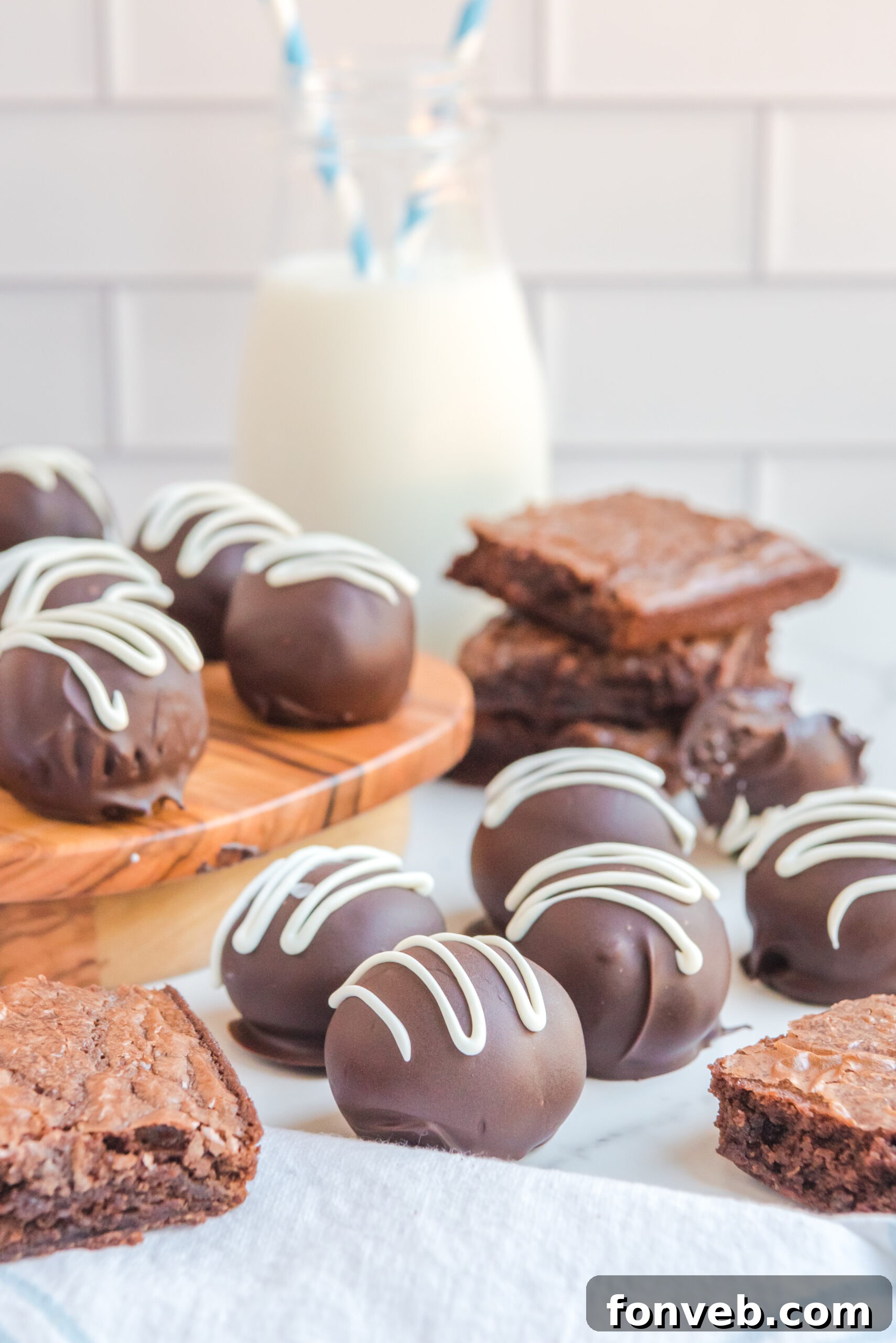 Decadent Brownie Bites 9 Brownie Bite Truffles on a white table with brownies stacked behind them and all around them