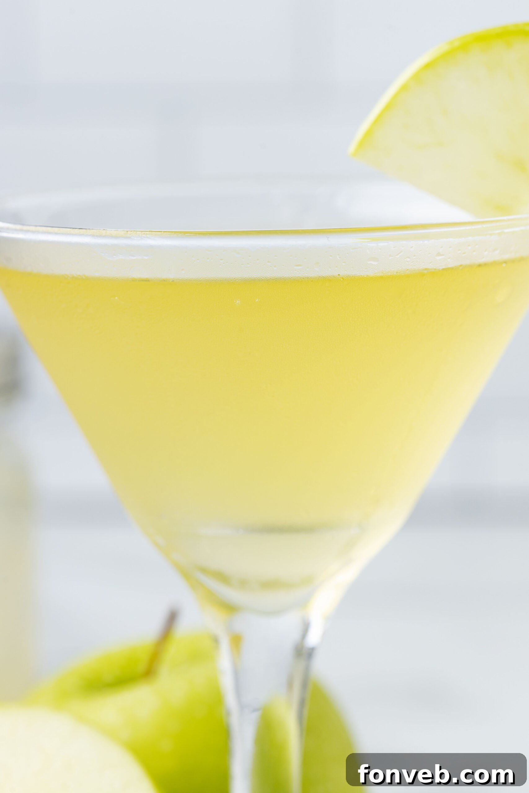 Close-up side view of an Appletini, showcasing the apple slice garnish in a martini glass.