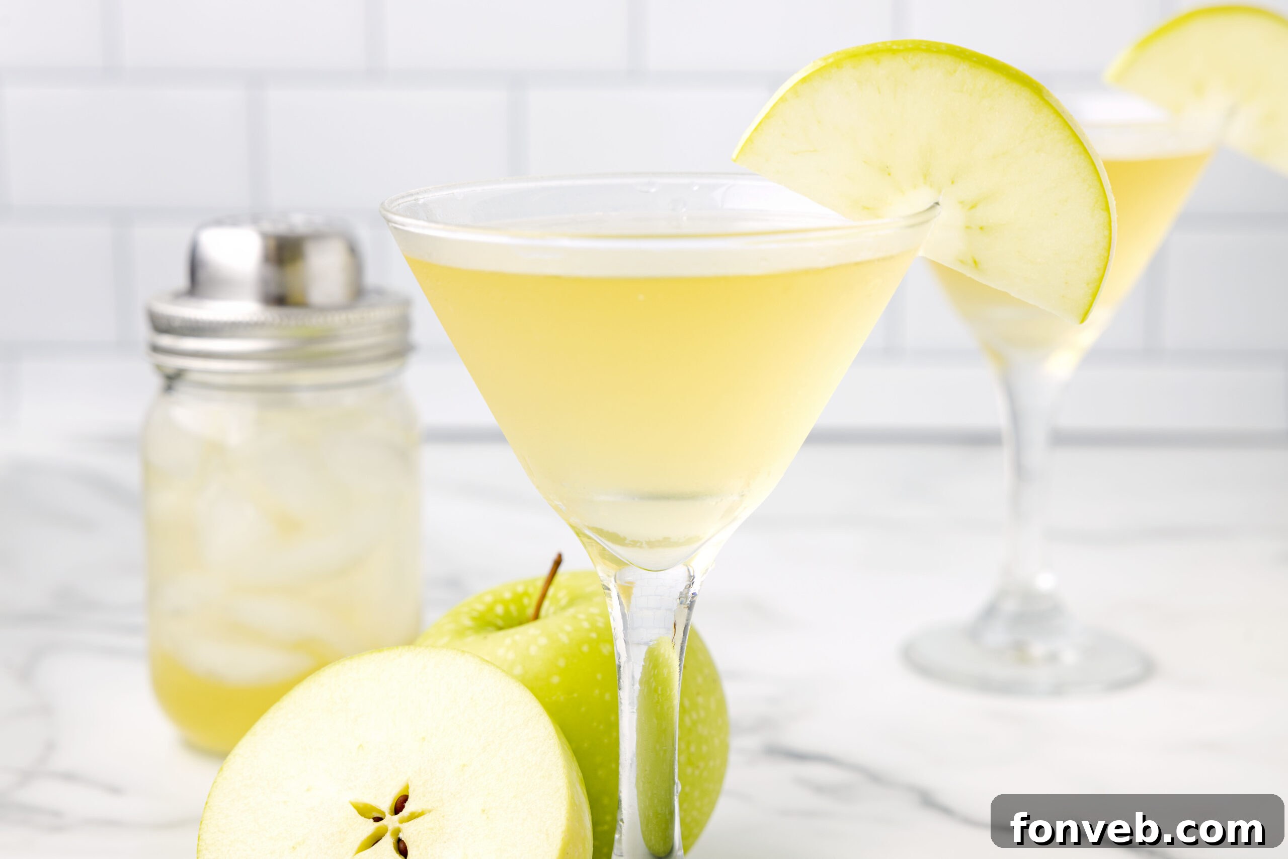 Close-up side view of an Appletini in a classic martini glass, accented with a thinly sliced green apple as garnish.