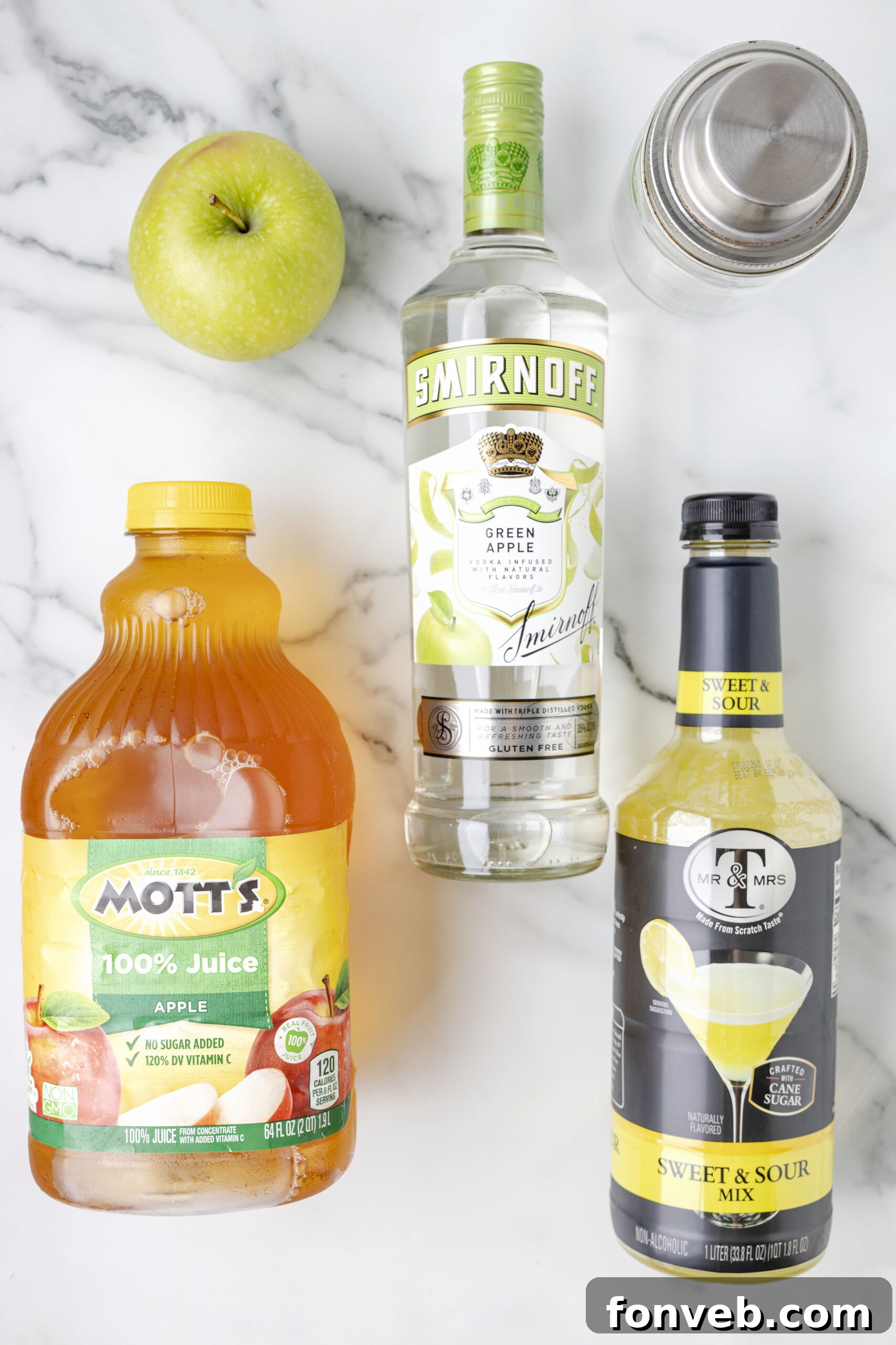 An overhead shot showcasing the ingredients laid out for making an Appletini cocktail, including apple vodka, apple juice, and sour mix bottles.
