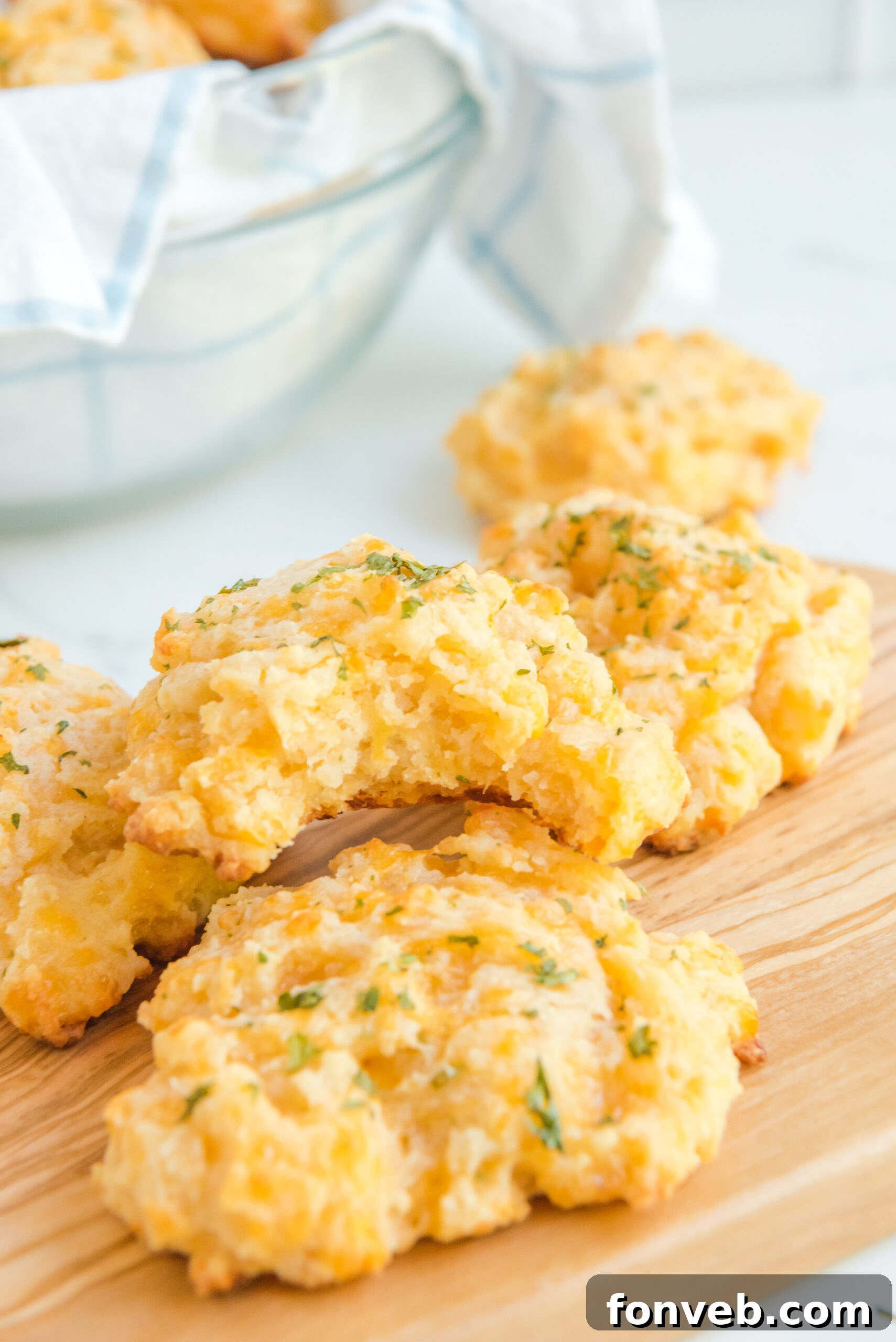 Side view of Copycat Red Lobster Cheddar Bay Biscuits with a bite taken out of one on a wooden cutting board, revealing the cheesy interior.