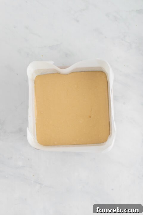 The finished Penuche Fudge mixture being poured into a parchment-lined baking dish.