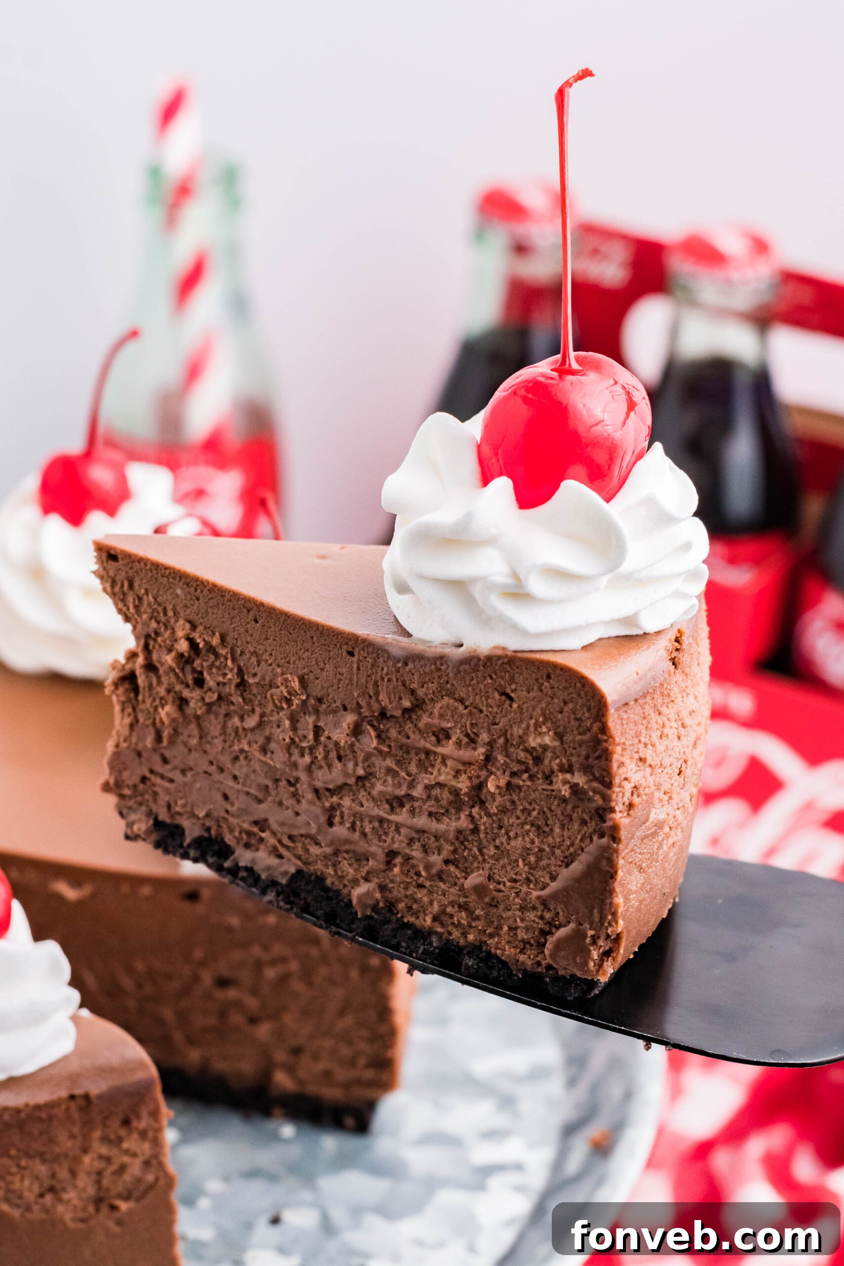 Side view of a slice of Coca Cola Cheesecake on a black cake server, showing the rich chocolate crust and creamy filling.