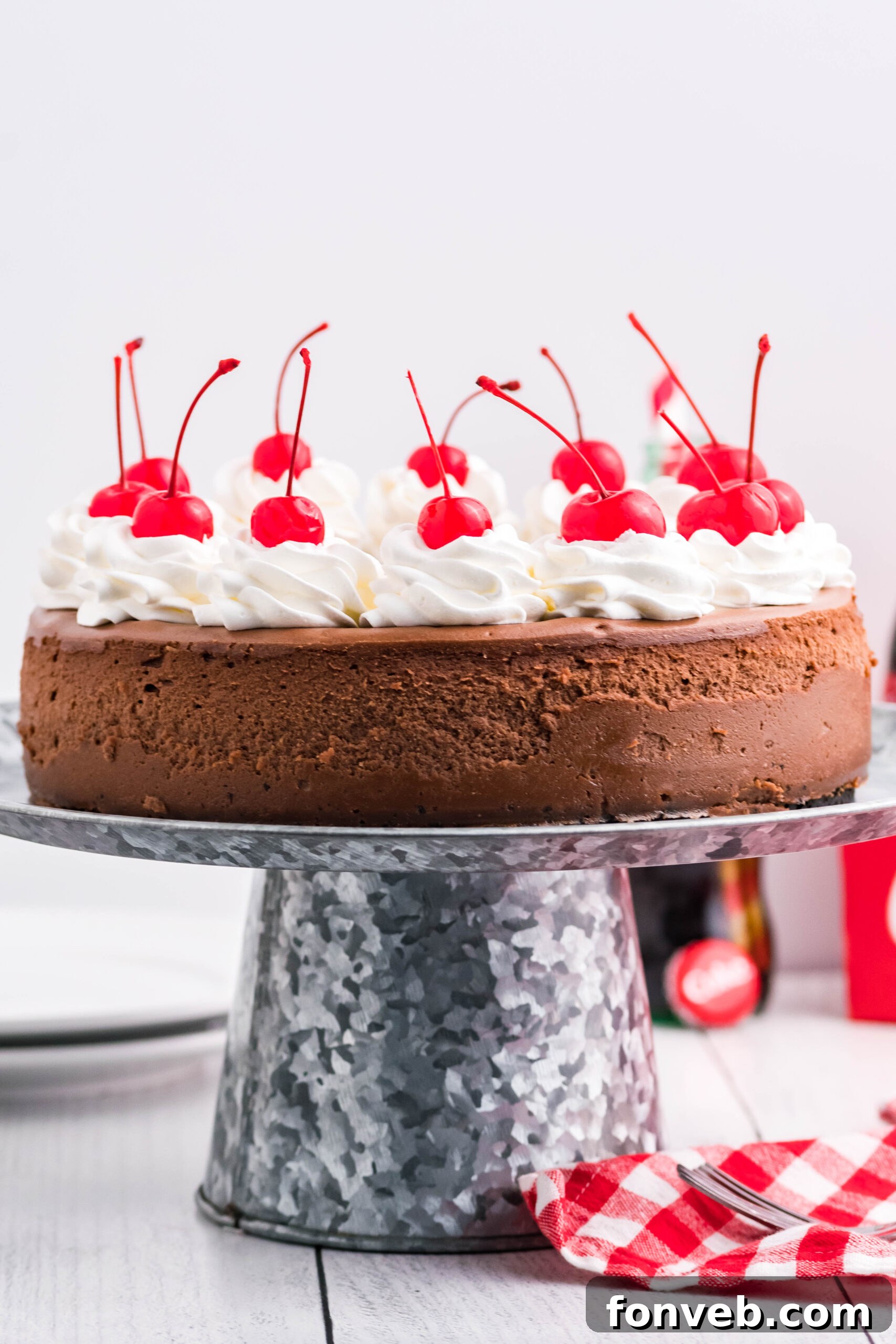 Side view of a whole Coca Cola Cheesecake on a galvanized cake pan, highlighting its smooth texture and dark chocolate hue.