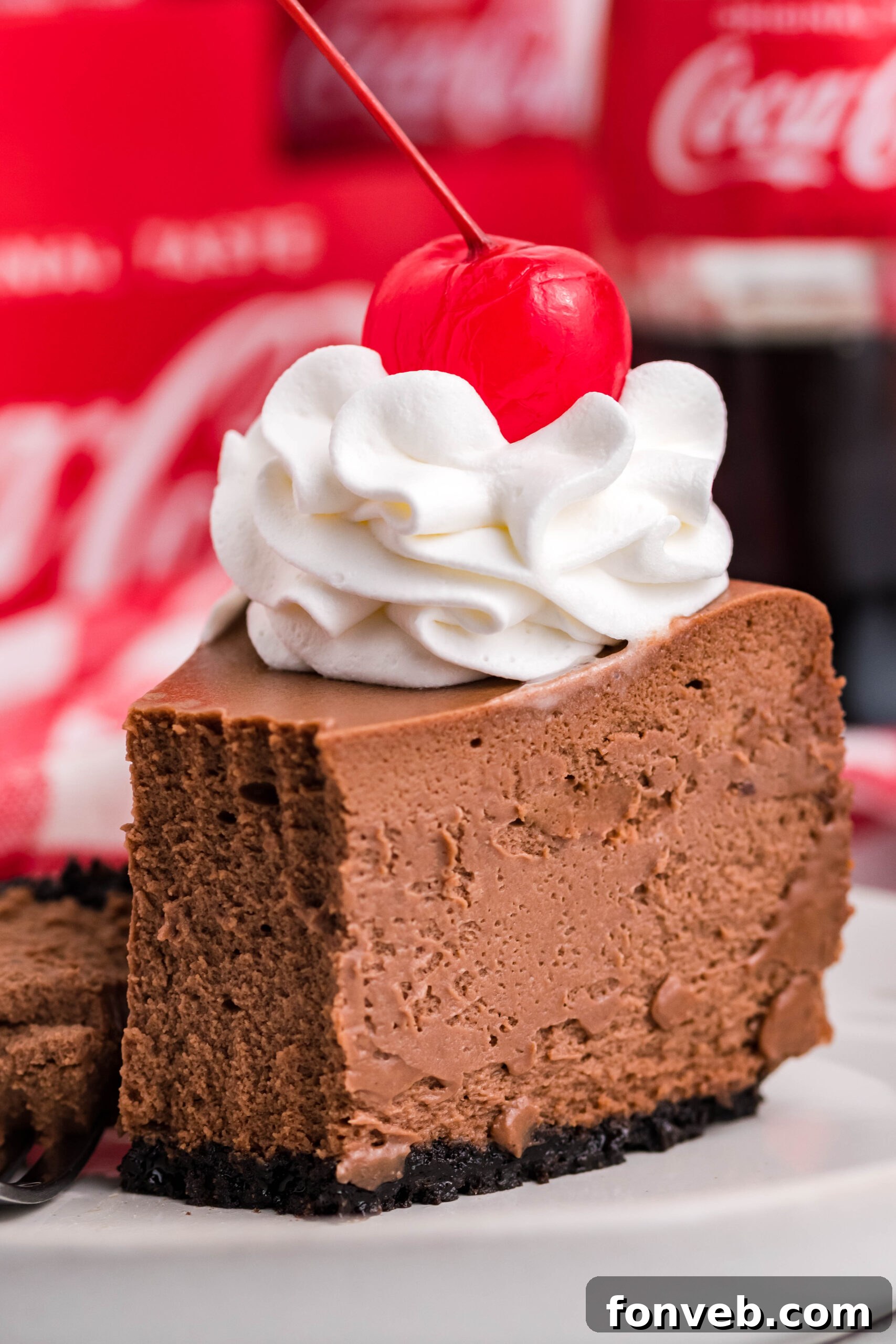 Coca-Cola Cheesecake slice on a white plate topped with whipped cream and a cherry, elegantly presented.