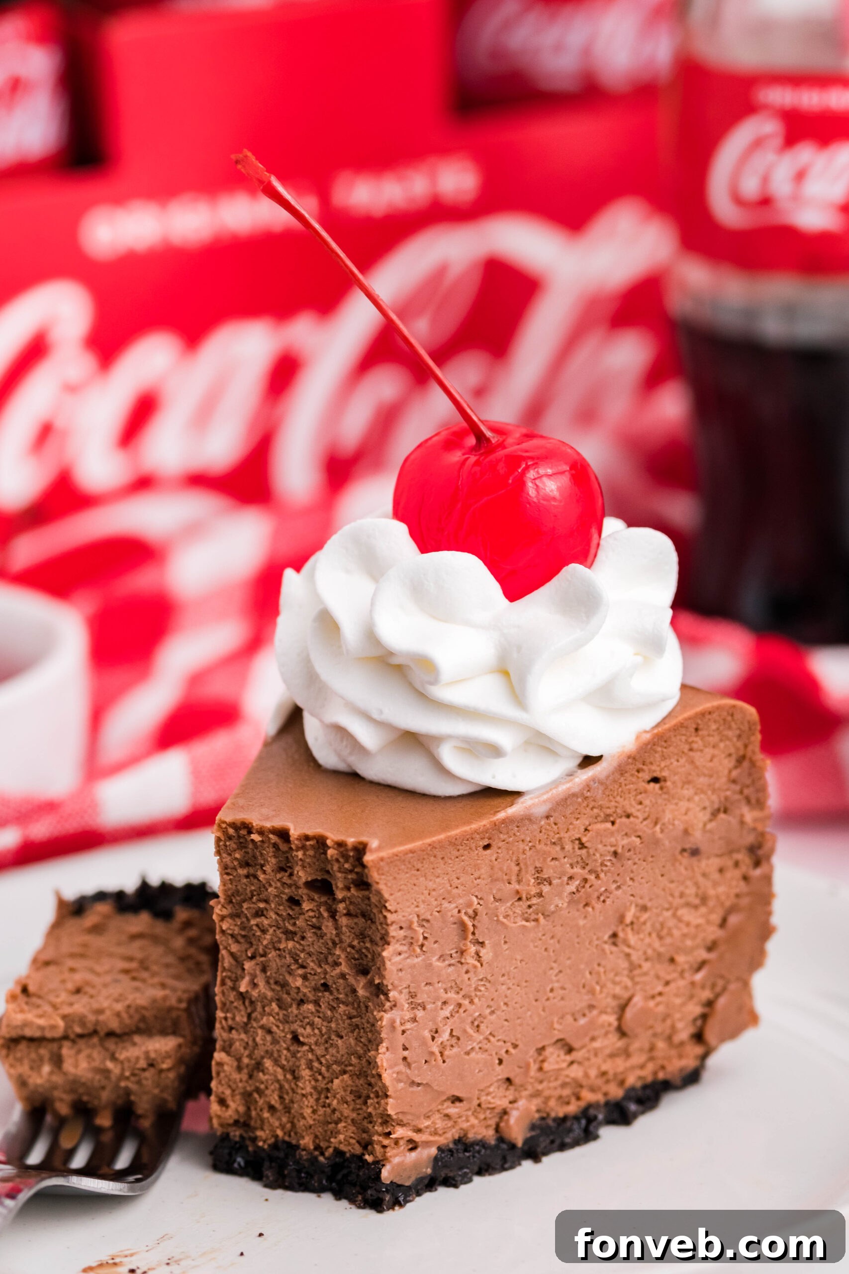 Side view of a slice of Coca Cola Cheesecake on a white dish with a piece removed and on a fork, highlighting the creamy texture.