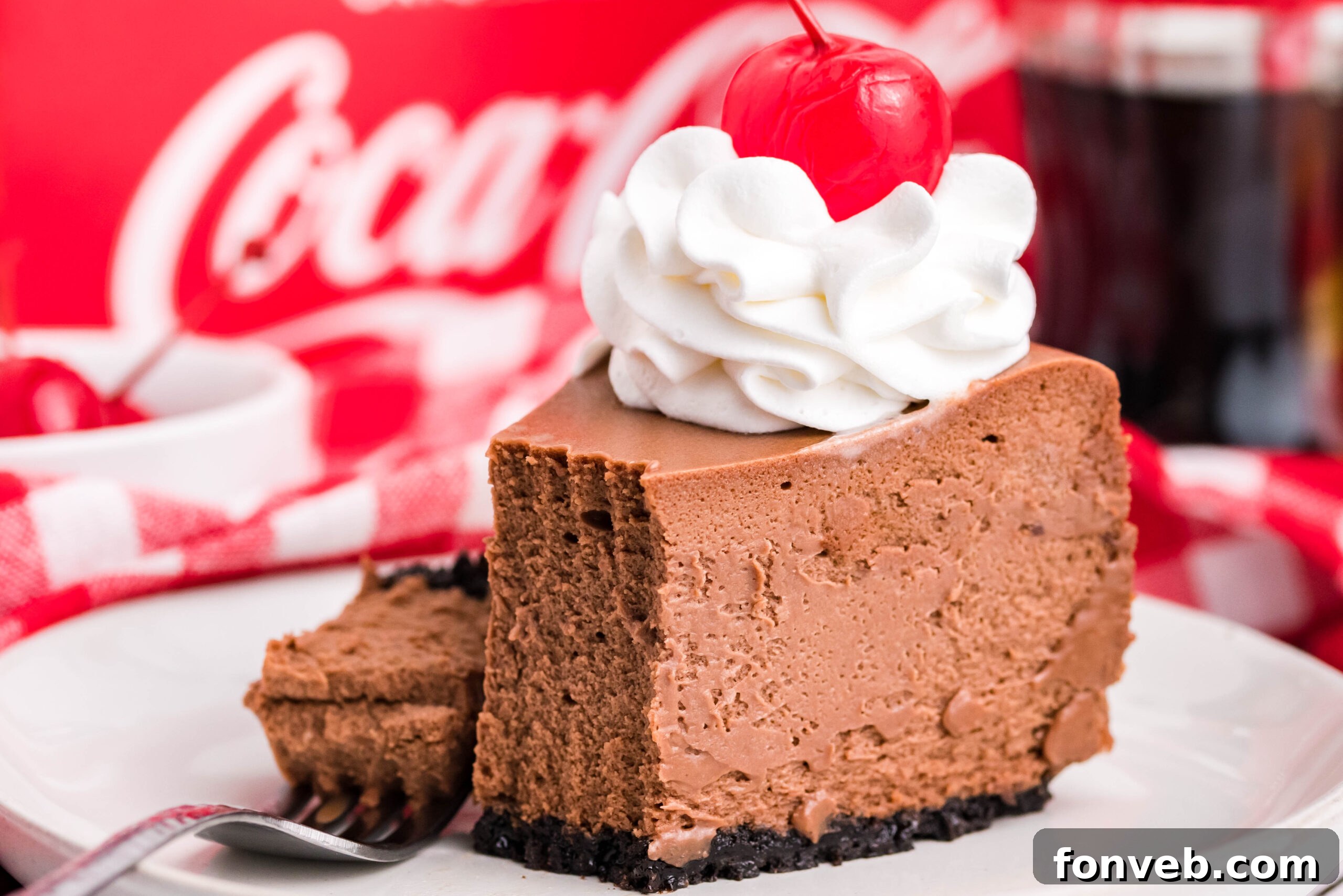 Side view of a slice of Coca Cola Cheesecake on a white dish with a piece removed and on a fork, showing the rich interior.