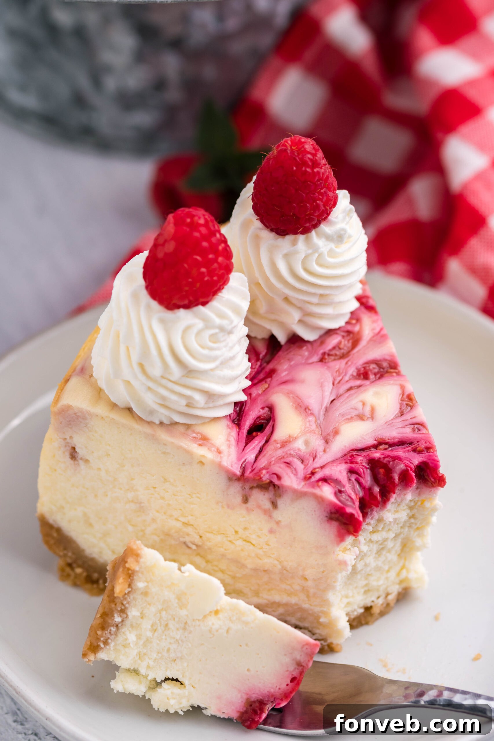 A slice of Raspberry Swirl Cheesecake on a white dish, with a bite playfully removed by a silver fork, highlighting its irresistible appeal.