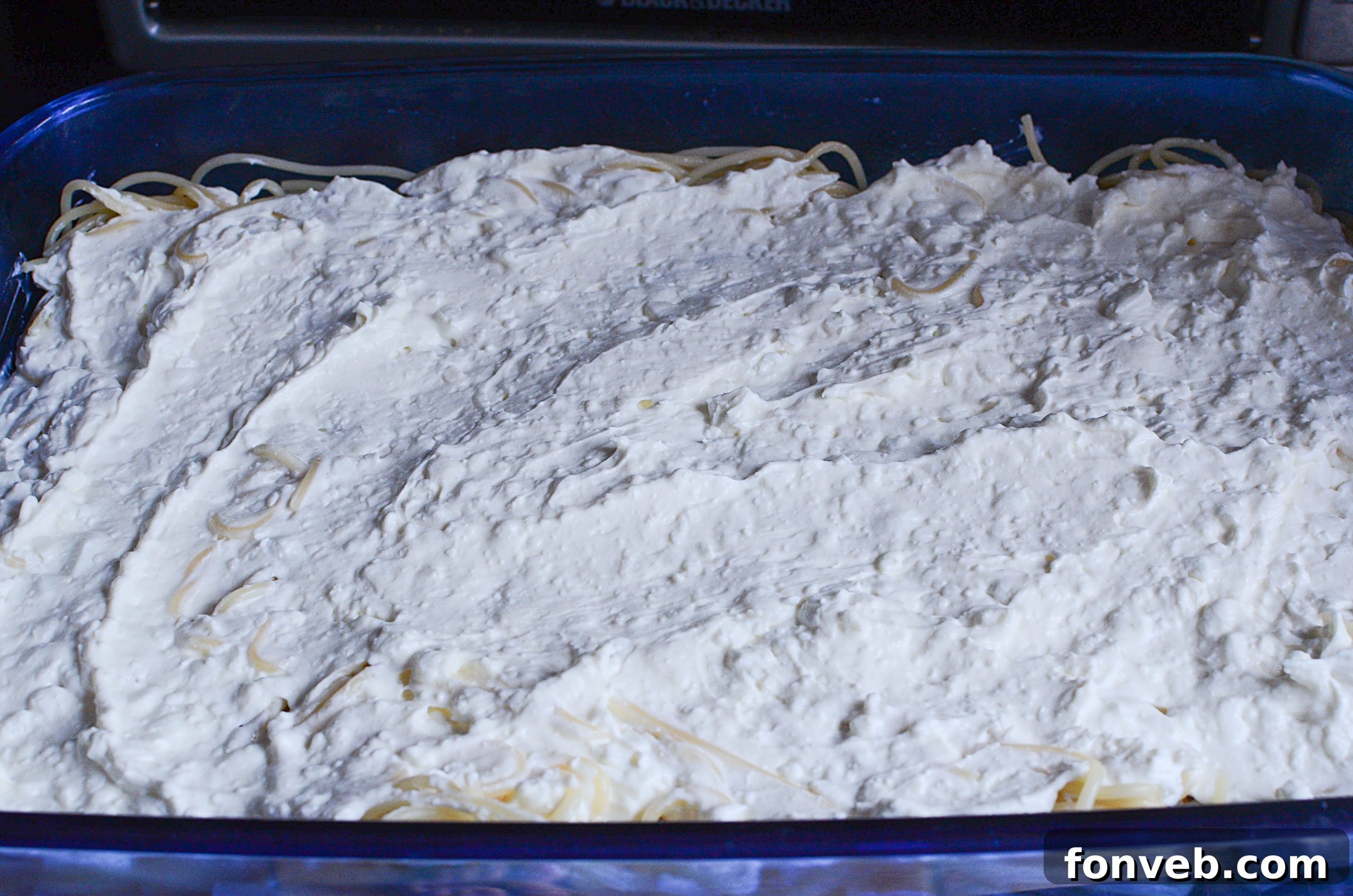 Meat sauce being spread over spaghetti in a casserole dish