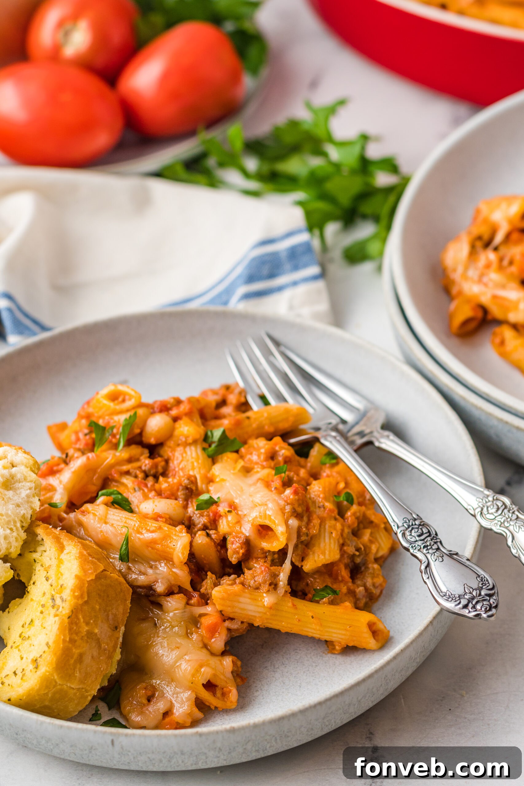 Pasta Fagioli Bake 14 Pasta Fagioli al Forno on a gray dish with a side of garlic bread and two silver forks, ready for a comforting meal.