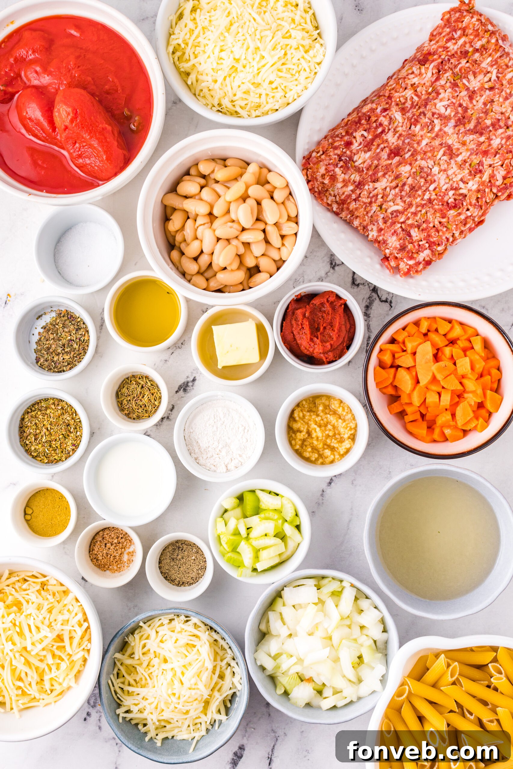 Pasta Fagioli Bake 7 Overhead view of various fresh ingredients laid out on a kitchen surface, including pasta, tomatoes, garlic, and fresh herbs.