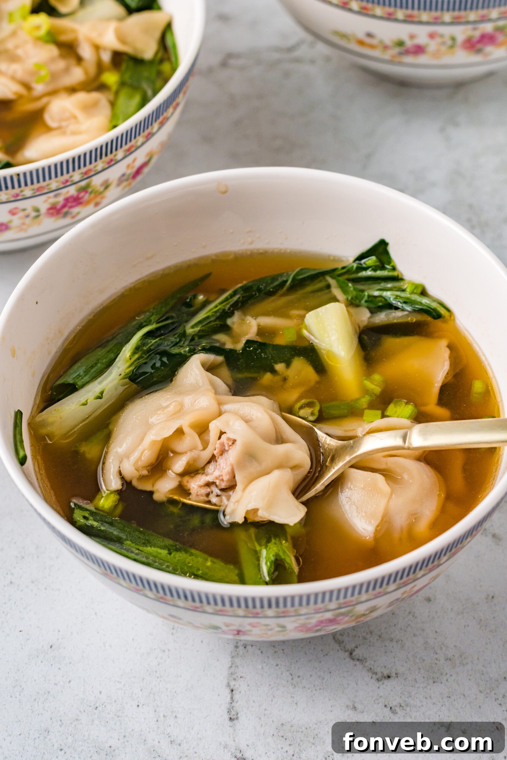 Comforting Wonton Soup 13 Wonton Soup in a white bowl with a gold spoon removing a bite.