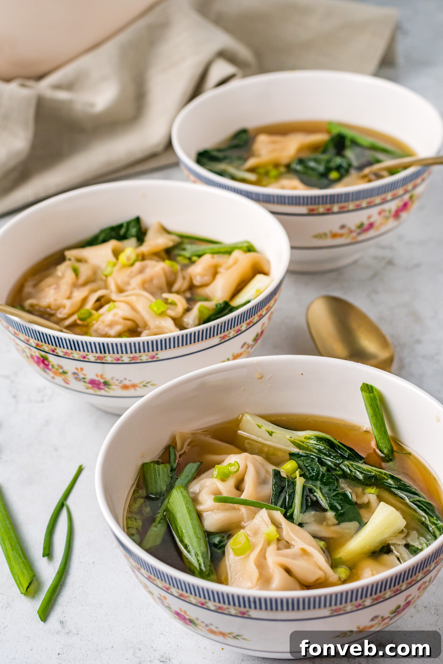 Comforting Wonton Soup 14 Side view of Wonton Soup in three white bowls topped with sliced green onion.