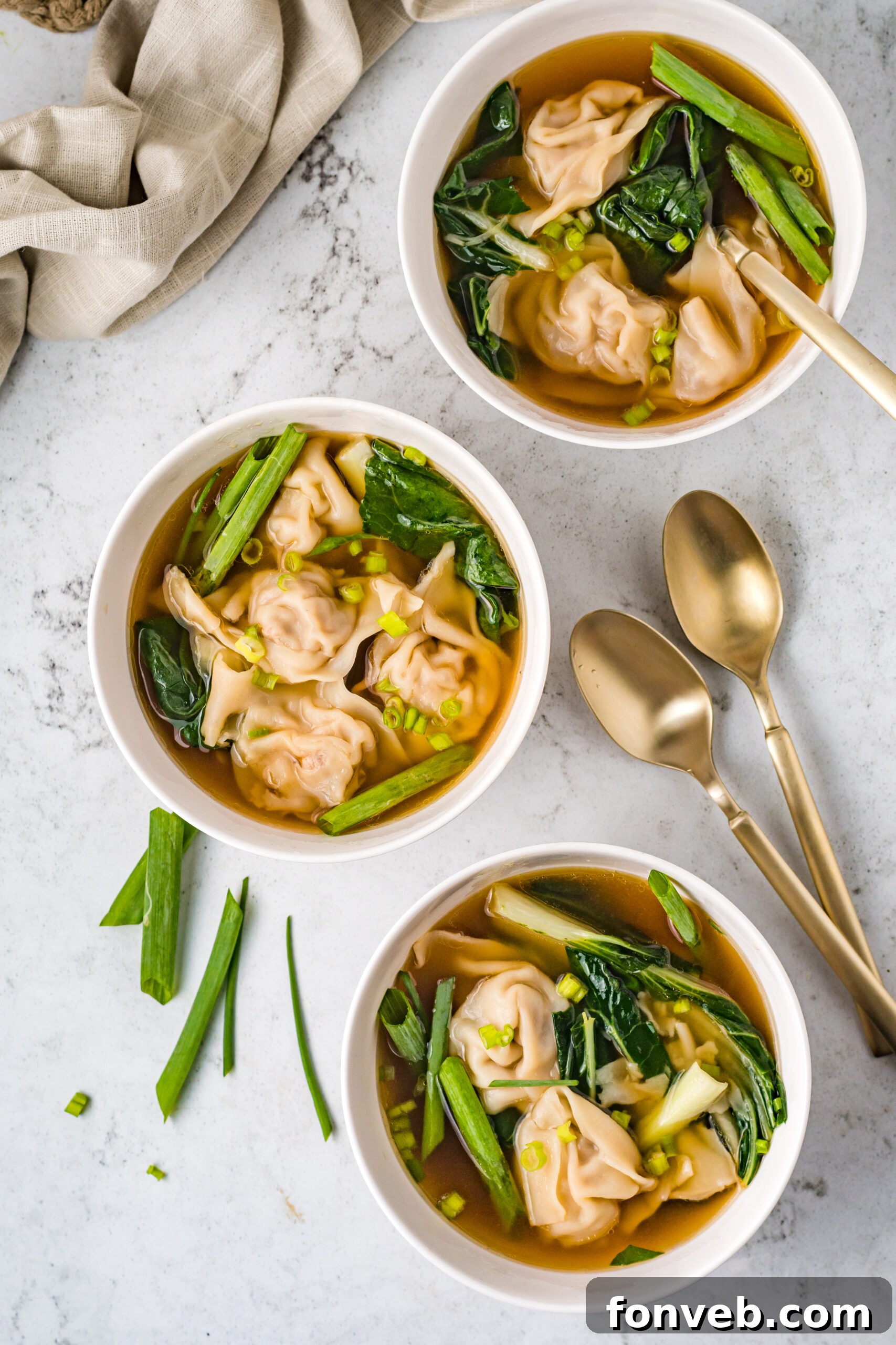 Comforting Wonton Soup 4 Overhead view of Wonton Soup in three white bowls topped with sliced green onion.