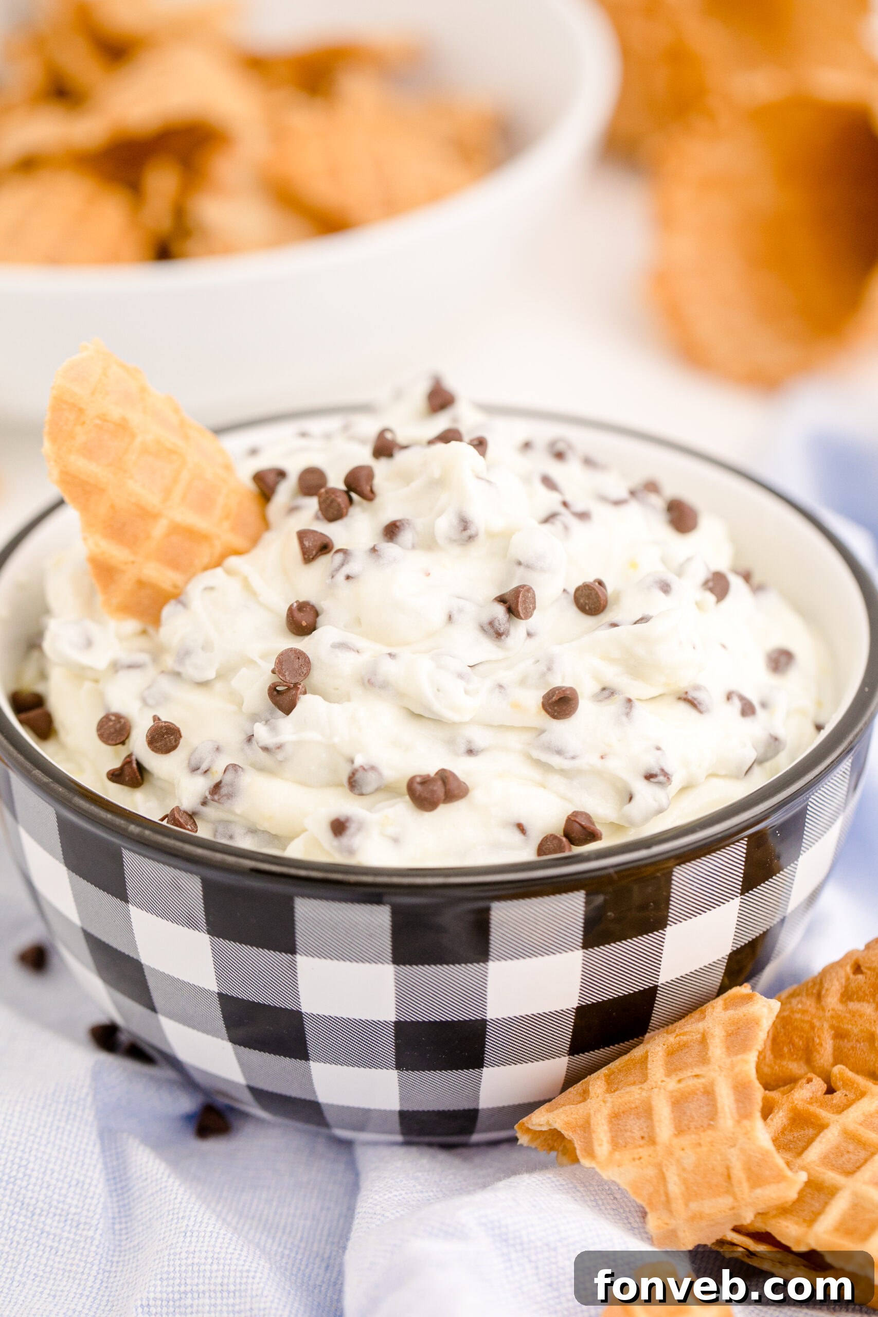 Close-up side view of creamy Cannoli Dip in a decorative black and white bowl, with a golden waffle cone ready for scooping.
