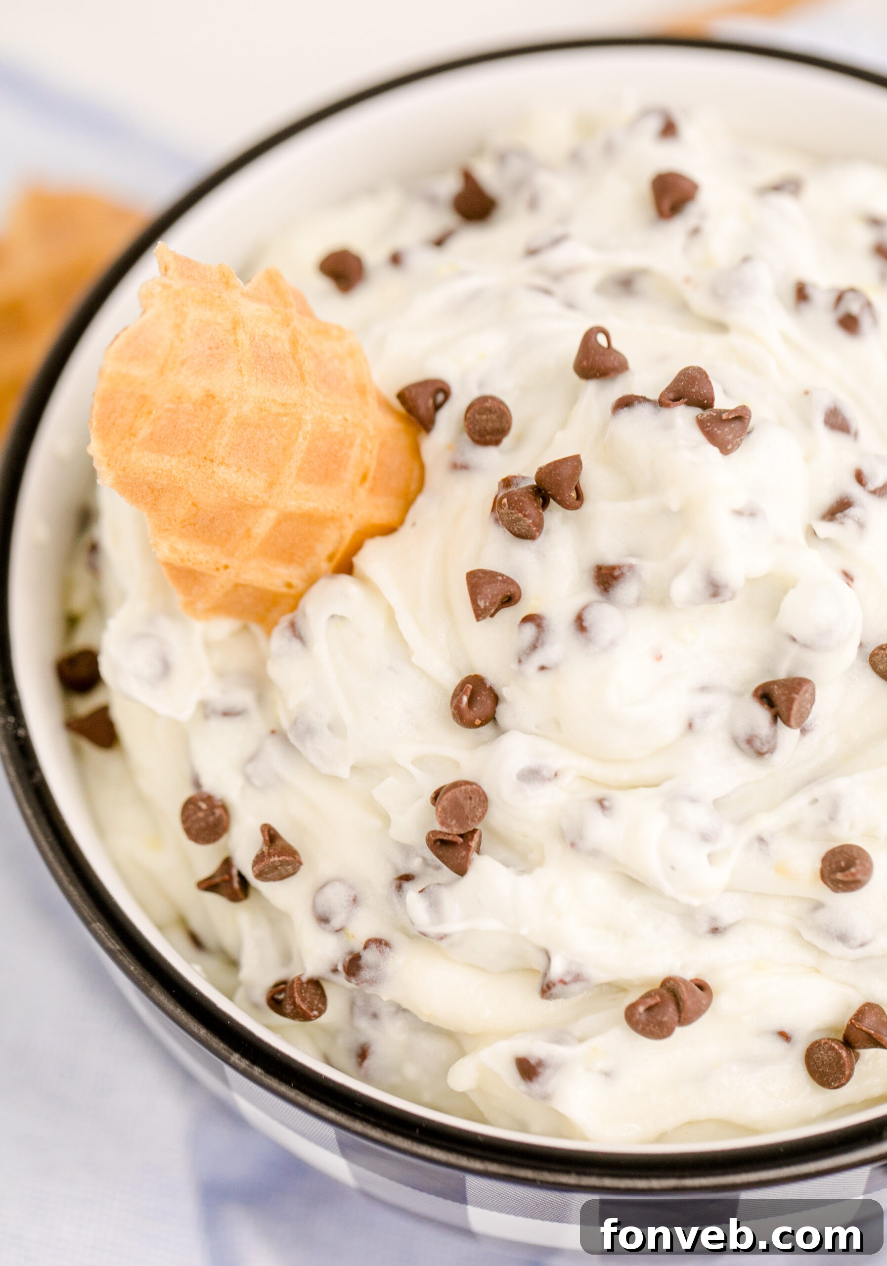 Overhead close-up of the textured Cannoli Dip, showing the mini chocolate chips and creamy ricotta, with a waffle cone for dipping.