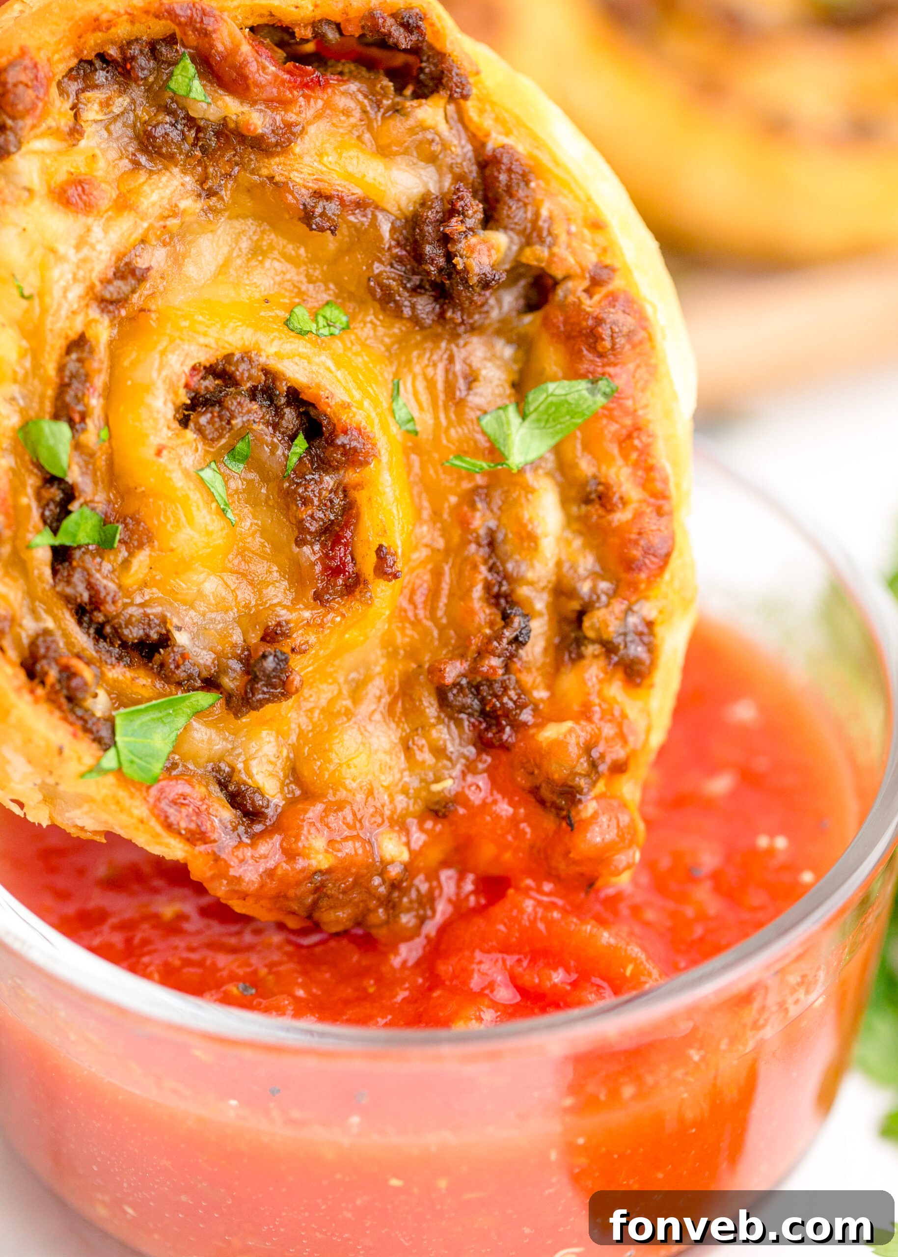 Up close view of Taco Pinwheel being dipped into a clear bowl filled with salsa.
