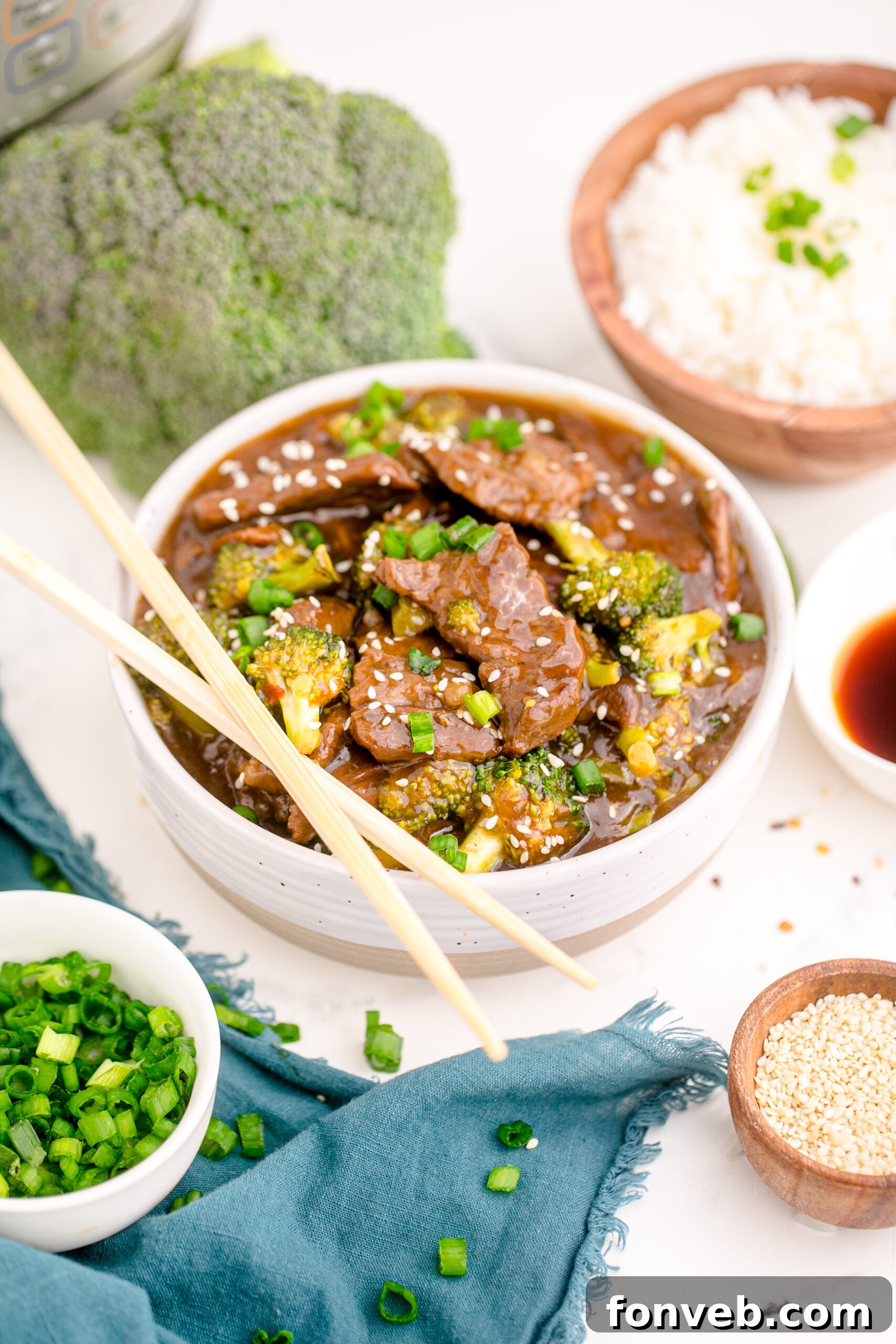 Side view of Instant Pot Beef and Broccoli in a white and tan bowl with a pair of chop sticks balanced on top of bowl.