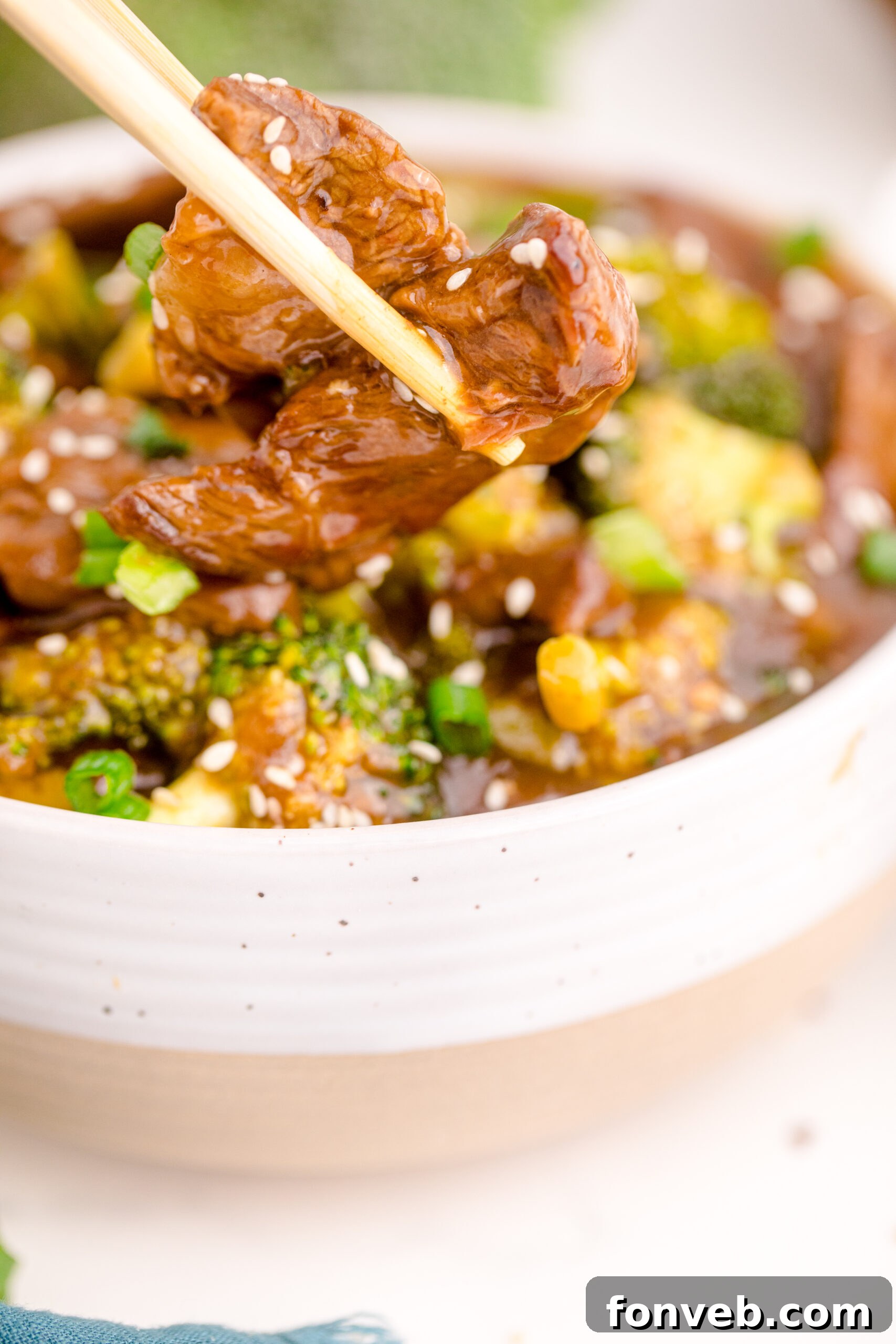 Up close view of chop sticks holding a piece of beef.