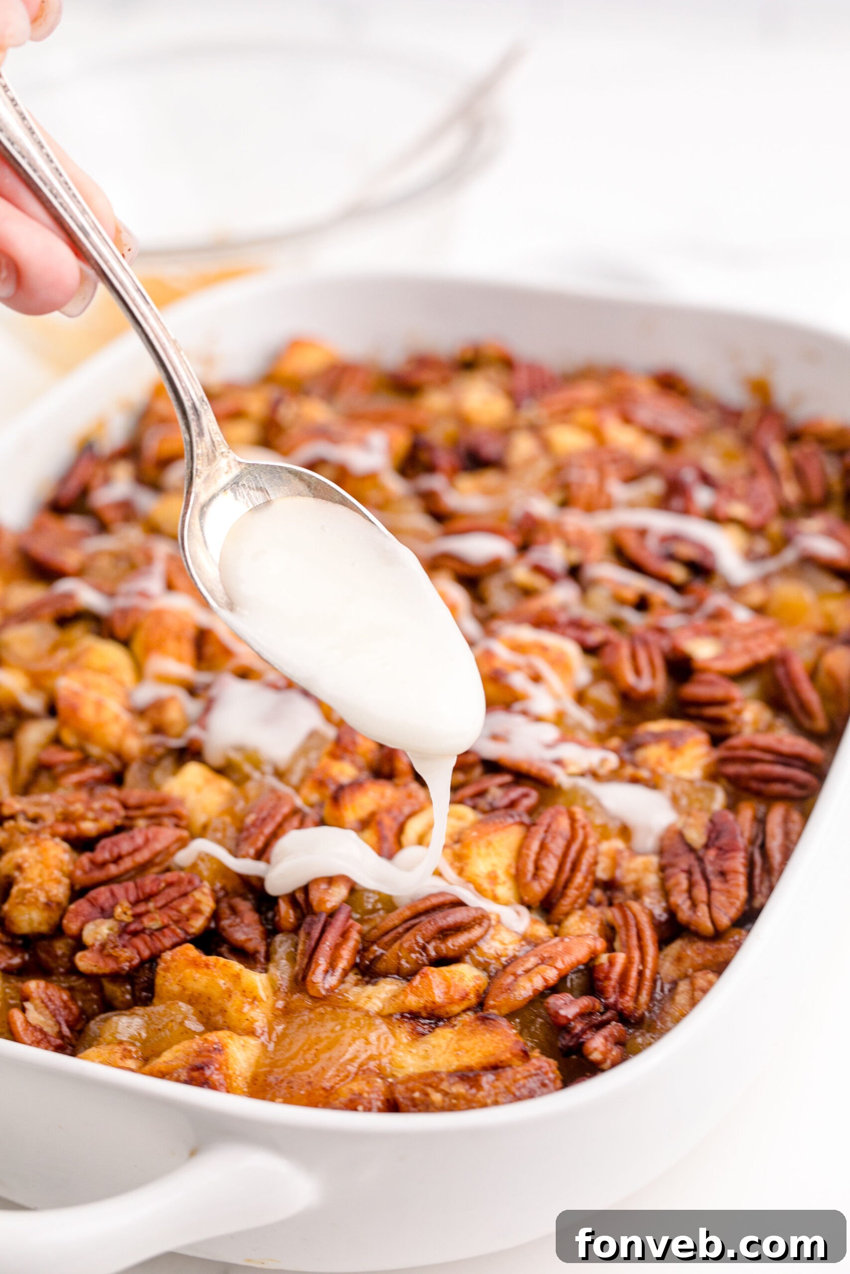 Irresistible Cinnamon Swirl Bake 15 Cinnamon Roll Casserole in a white baking dish with a spoon drizzling icing on top