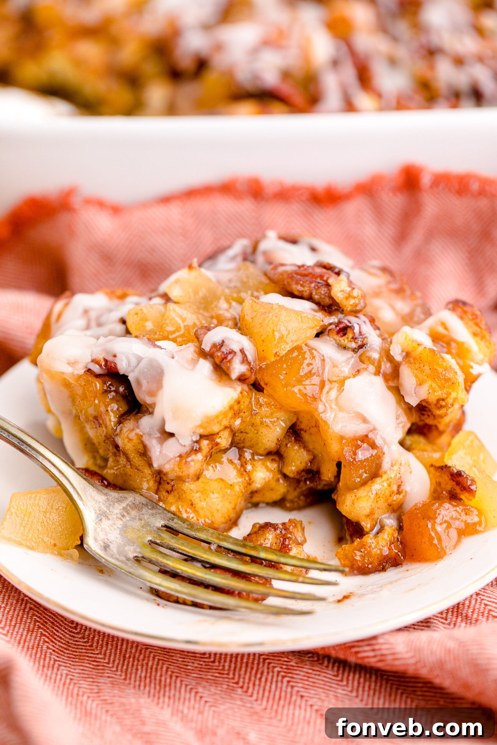 Irresistible Cinnamon Swirl Bake 17 Cinnamon Roll Casserole on a white plate with a gold fork removing a bite.