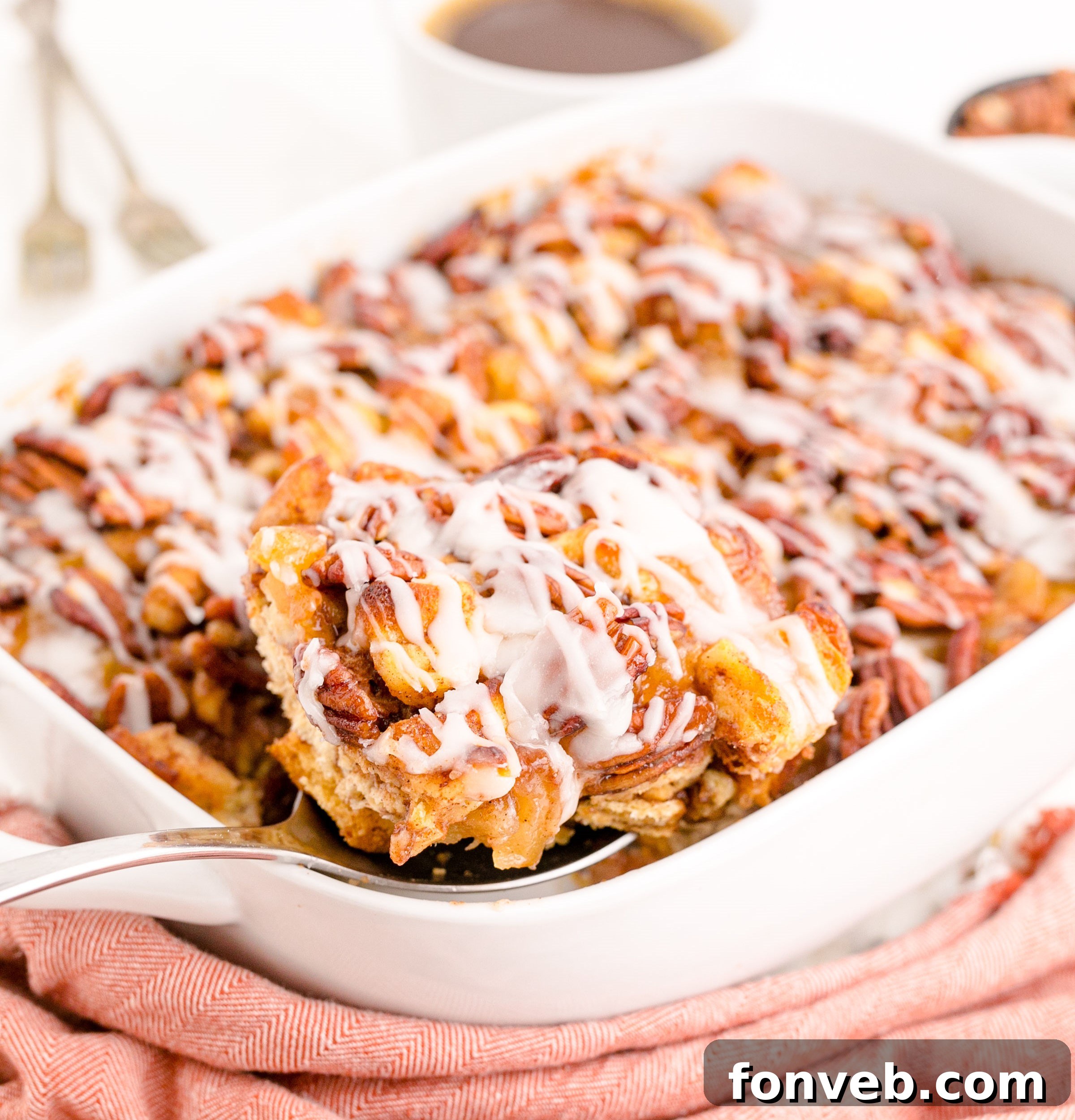 Irresistible Cinnamon Swirl Bake 3 A silver spoon removing a serving of cinnamon roll casserole from a white baking dish.