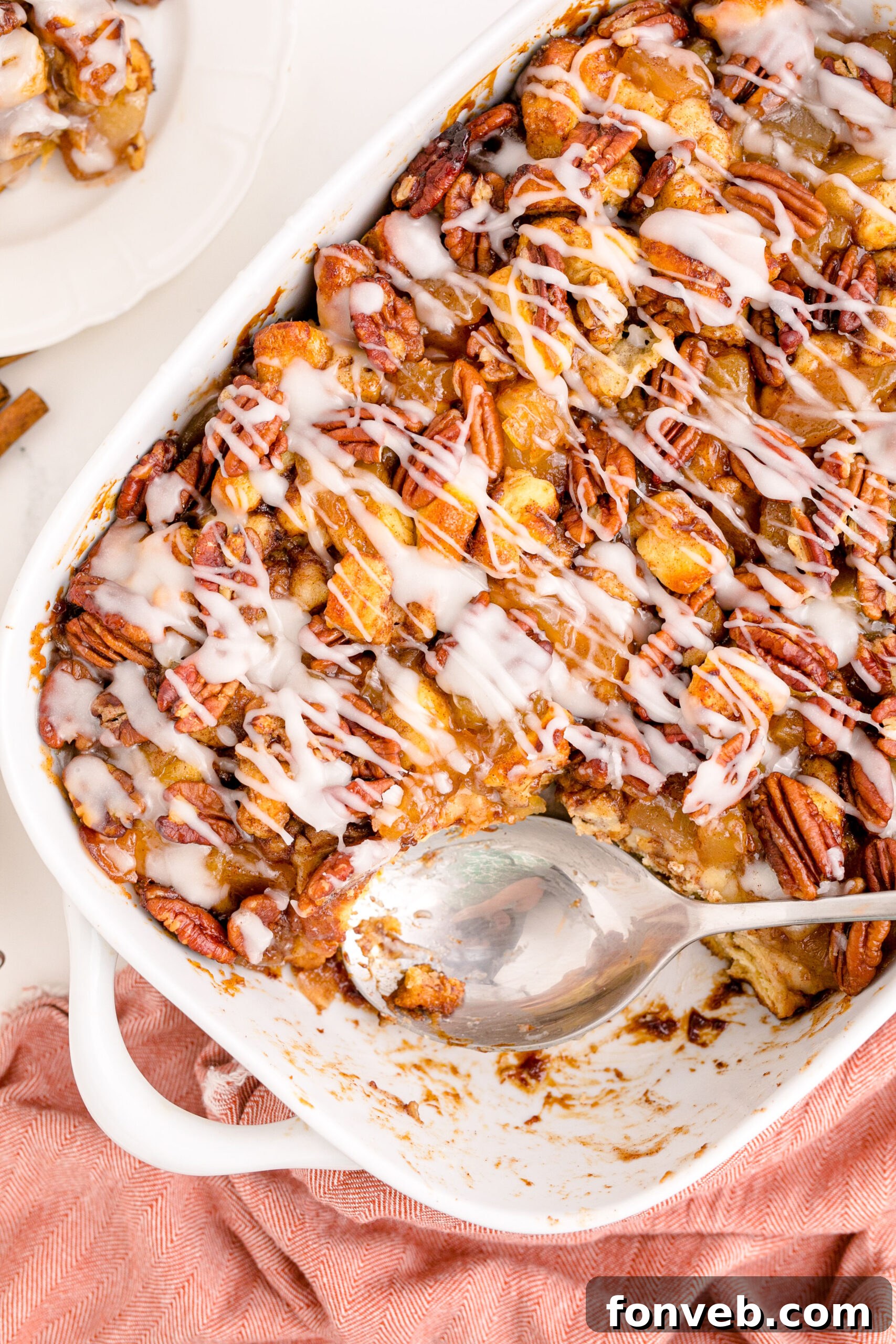 Irresistible Cinnamon Swirl Bake 4 Overhead view of A silver spoon removing a serving of cinnamon roll casserole from a white baking dish.