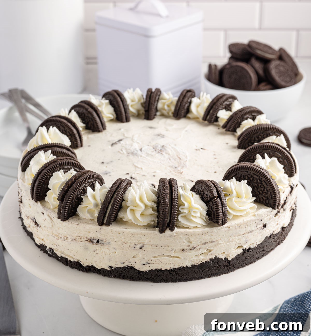 no bake oreo cheesecake on a white cake stand unsliced, ready to be served.