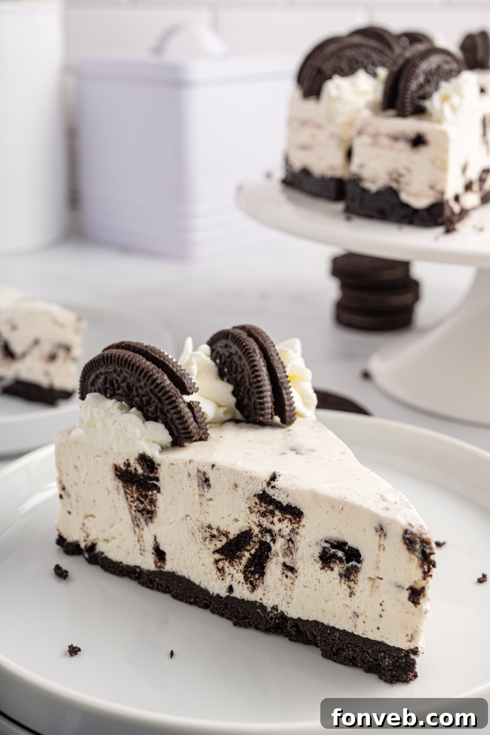 Side view of a slice of No Bake Oreo Cheesecake on a white dish, garnished with whipped cream and an Oreo half.