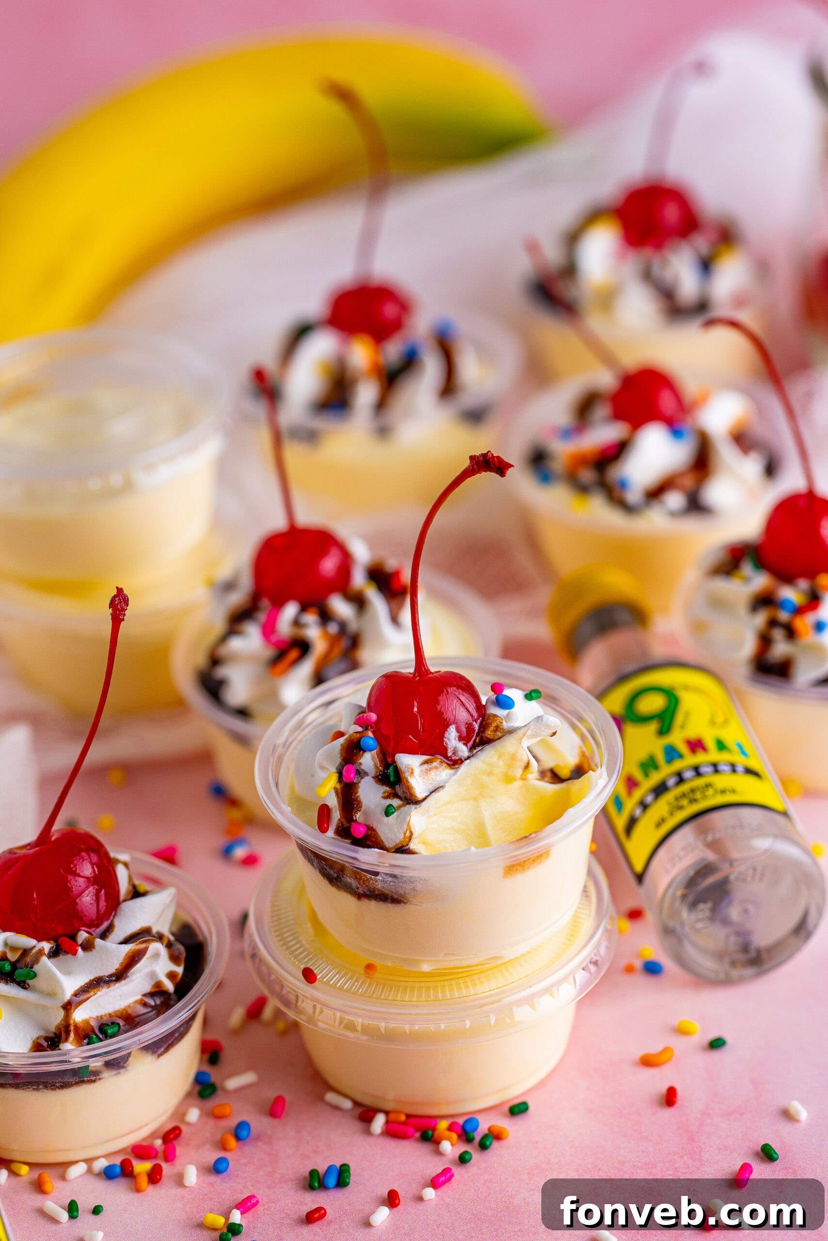 Mini Banana Split Delights 16 Banana pudding shots stacked high, surrounded by festive sprinkles, ready for a party.