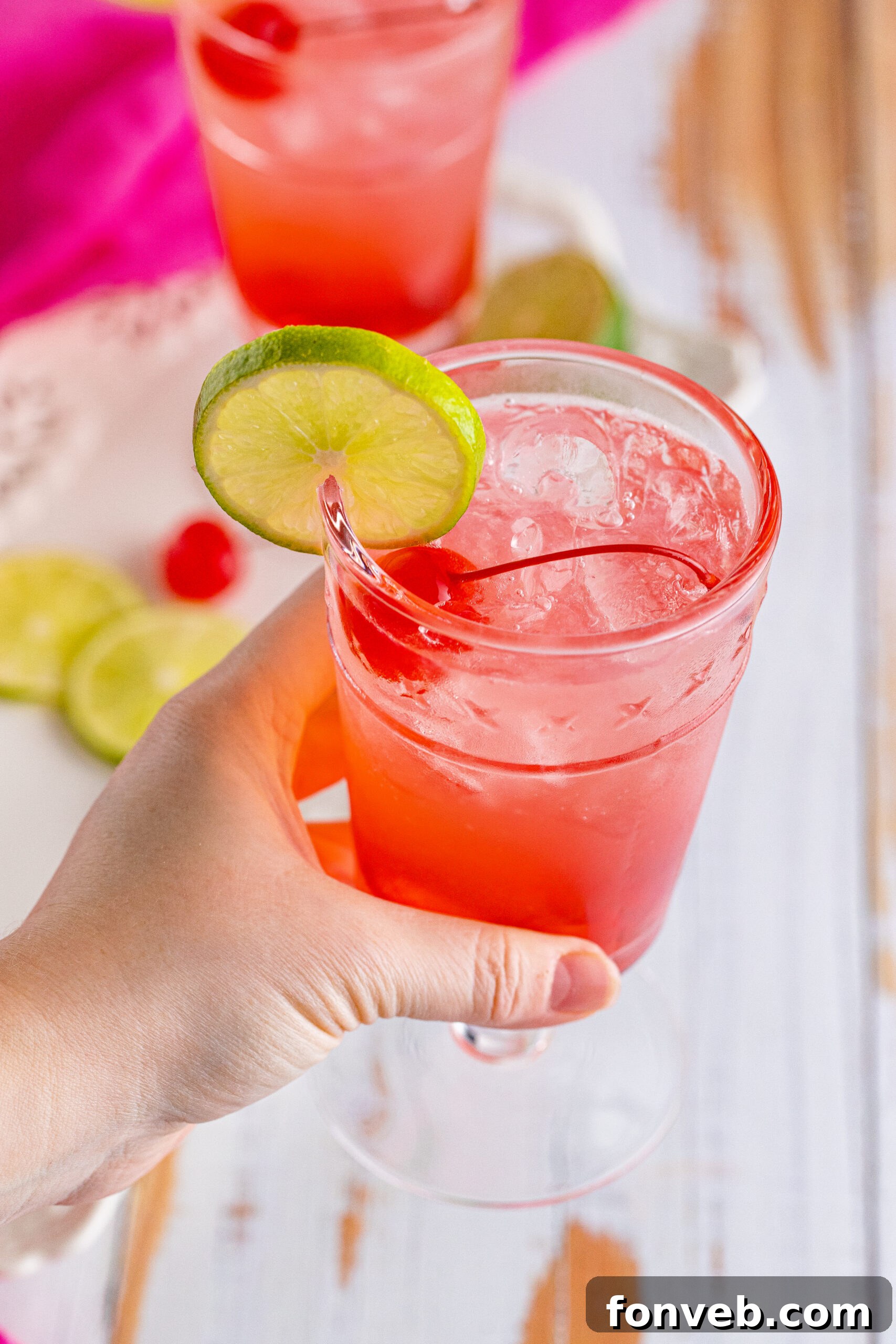 45-degree view of a hand holding a Dirty Shirley Temple garnished with a lime slice.