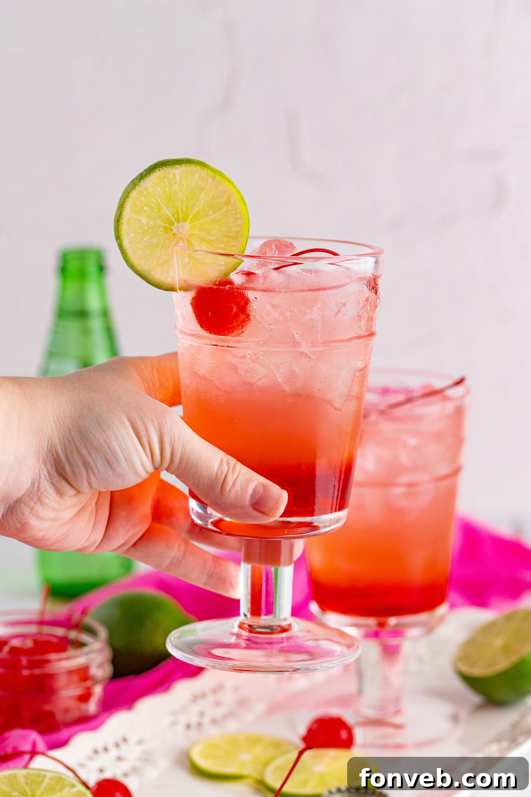 Side view of a hand holding a Dirty Shirley Temple garnished with a lime slice.