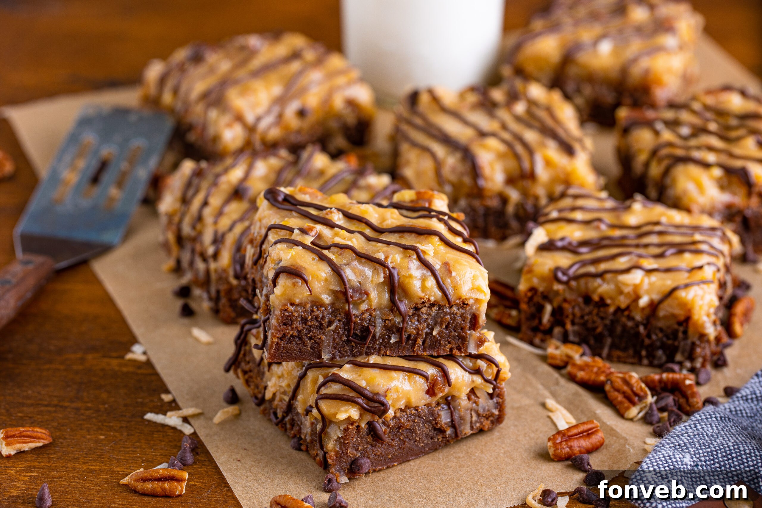 German Chocolate Brownies on a wood table, surrounded by chopped pecans and chocolate chips, arranged for a tempting presentation.