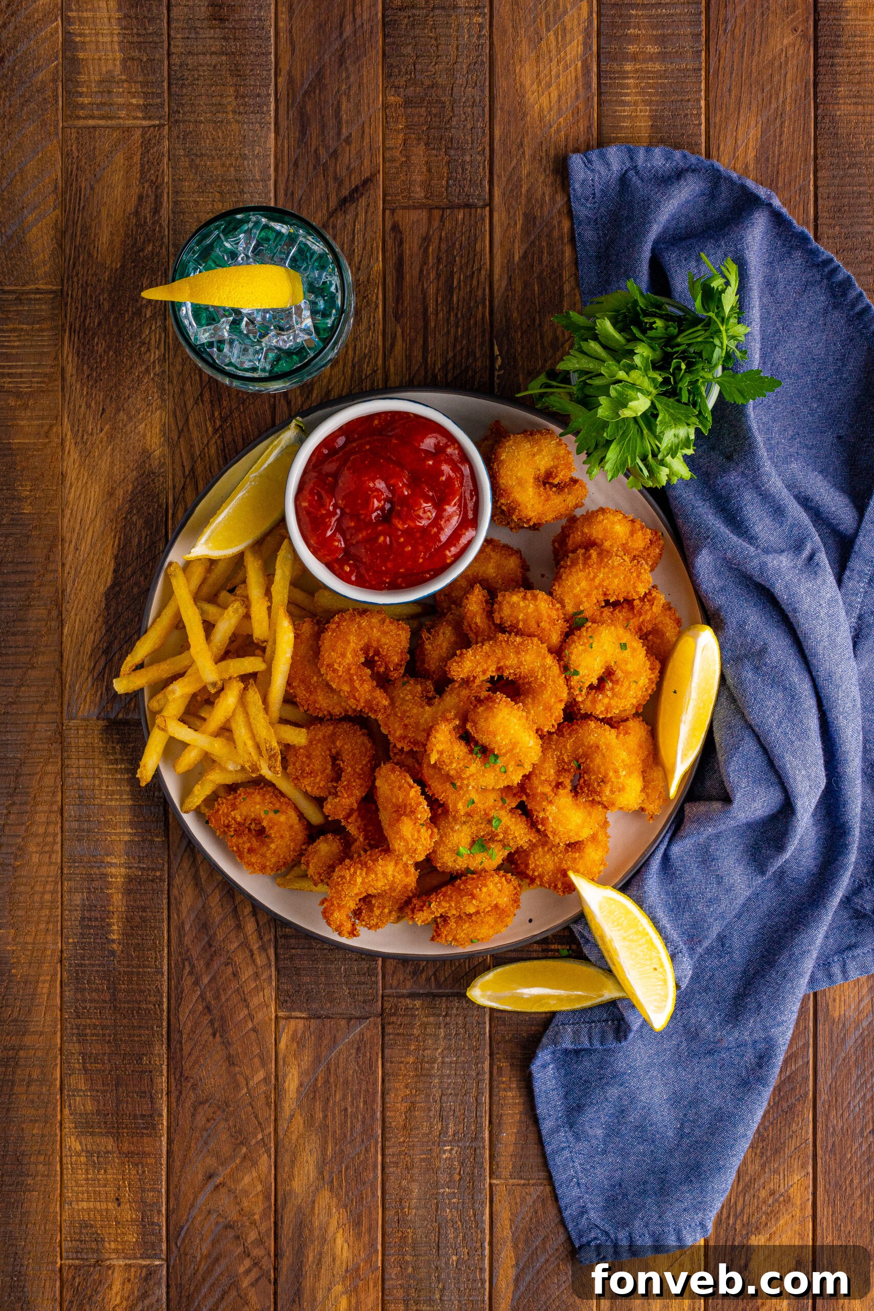 Overhead view of Panko Fried Shrimp  on a dish served with french fries, cocktail sauce and lemon wedges.