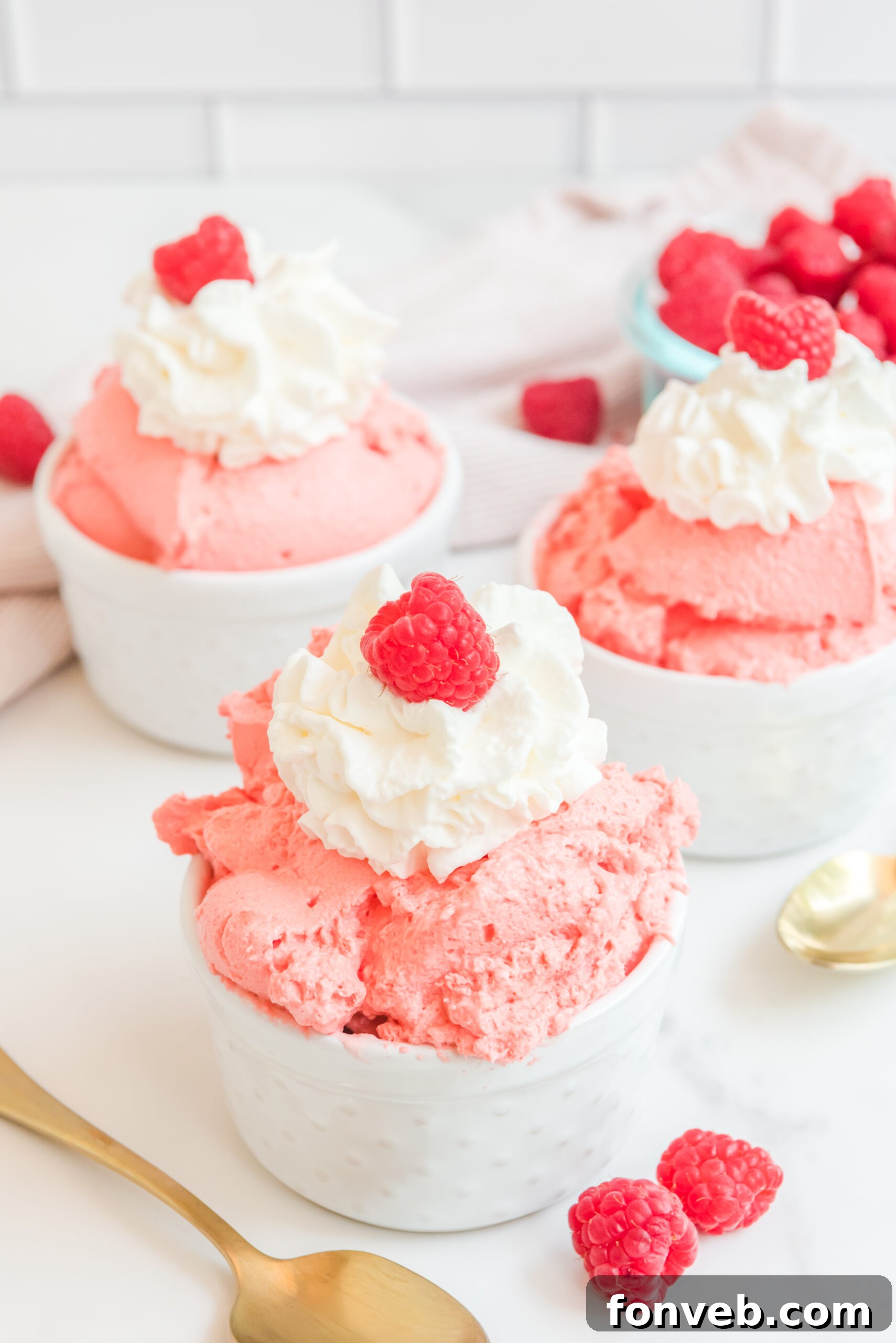 Luscious Raspberry Whip 15 Raspberry Fluff in a white bowl topped with whipped cream and a raspberry, with a gold spoon resting beside it.